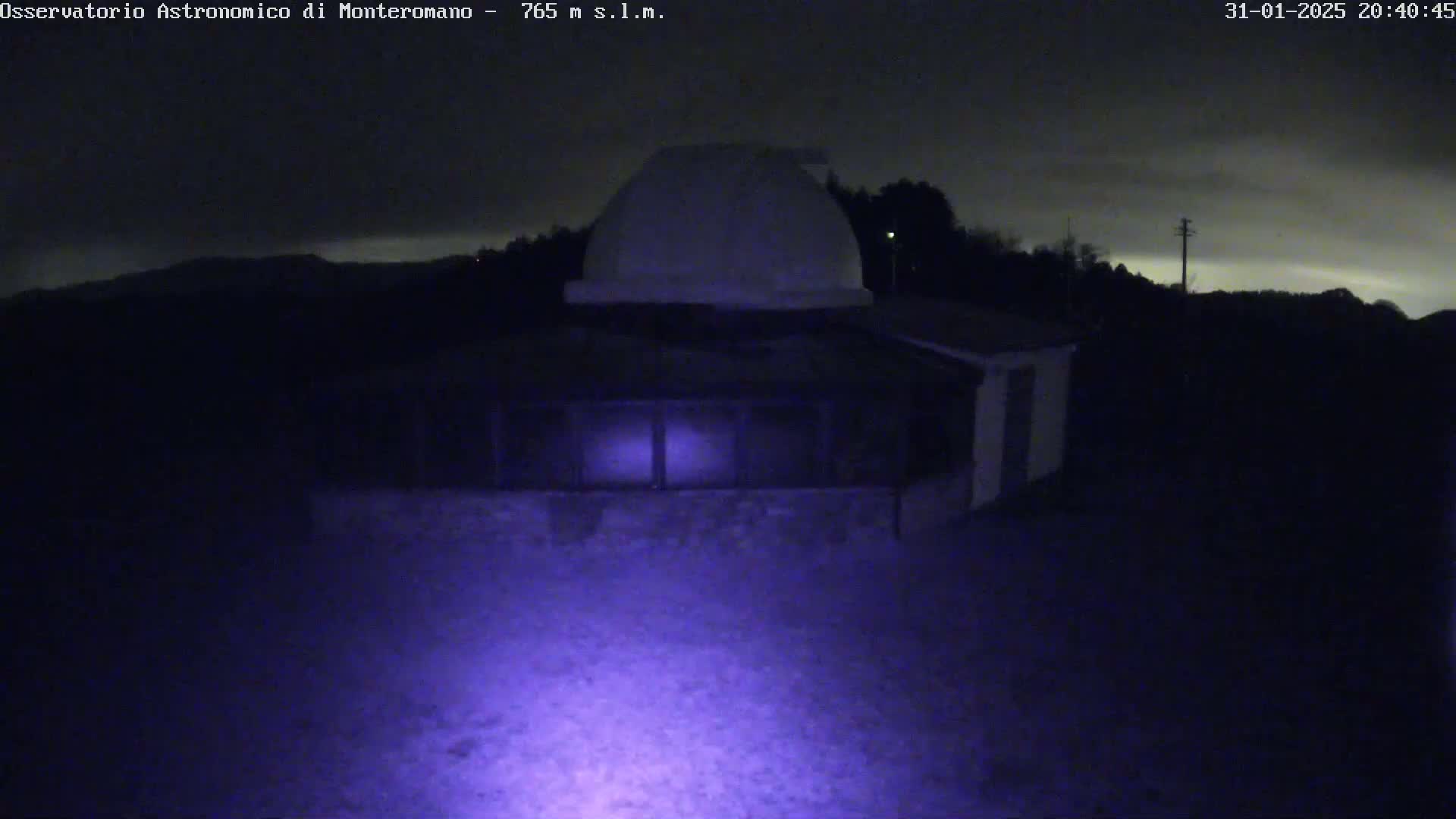 A nighttime view of a white dome-shaped building with a lower structure, under a cloudy sky.