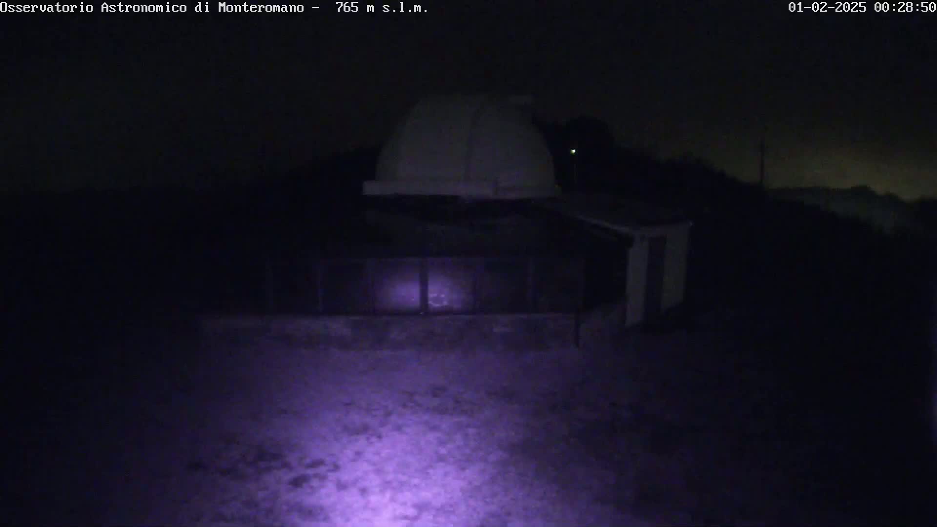A white dome-shaped structure is visible at night under a dark, possibly cloudy sky, illuminated by a purple-hued light source.