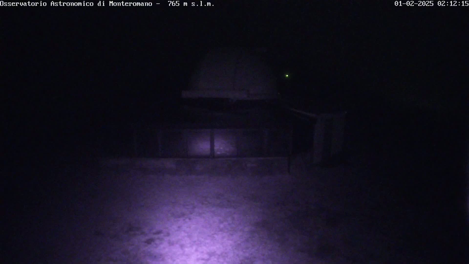 A low-light nighttime image shows a dark structure, possibly a building or observatory dome, illuminated by a light source in the foreground.