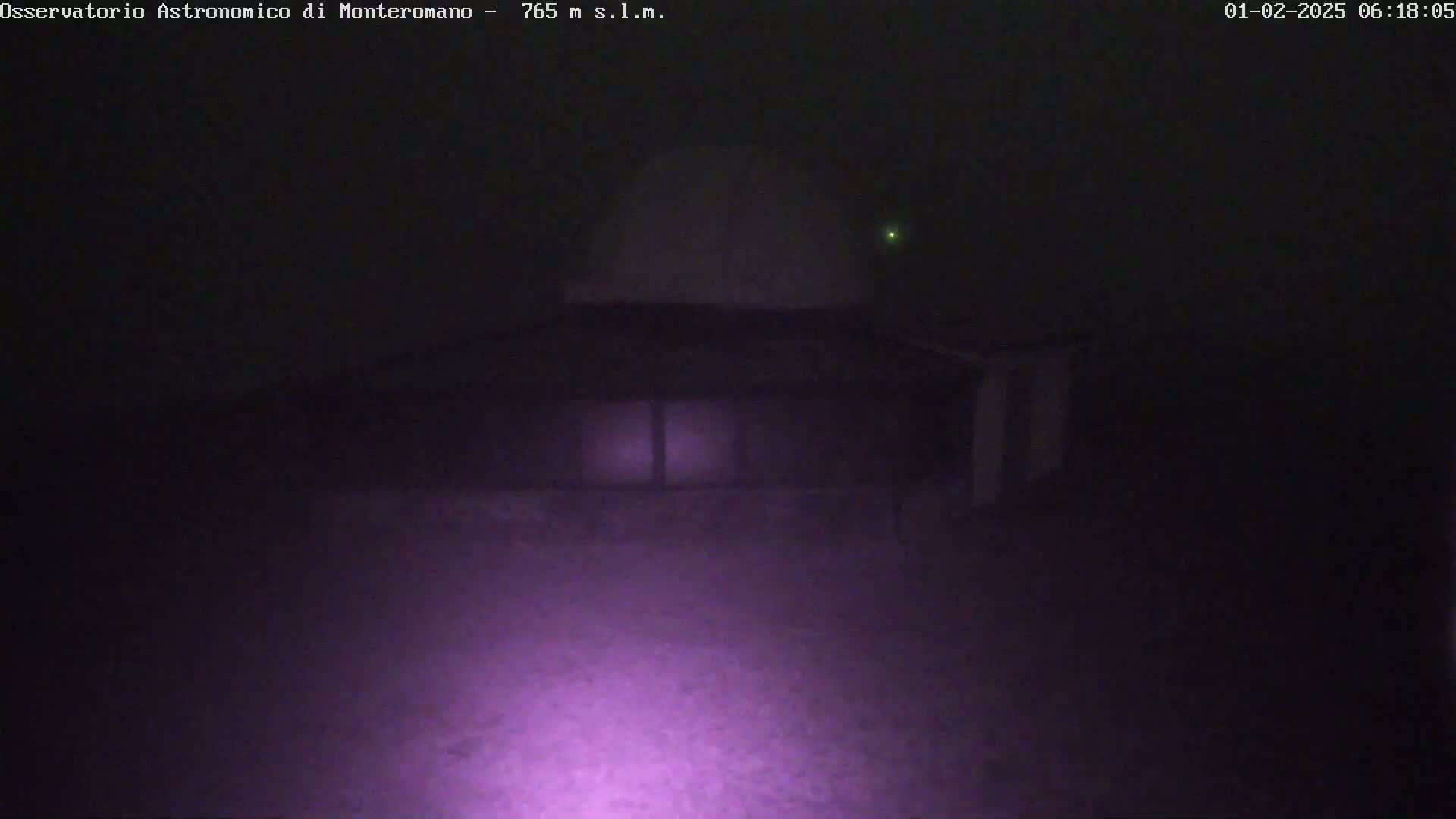 A low-light nighttime image shows a building with a dome-shaped roof and windows, possibly an observatory, under hazy or foggy conditions.
