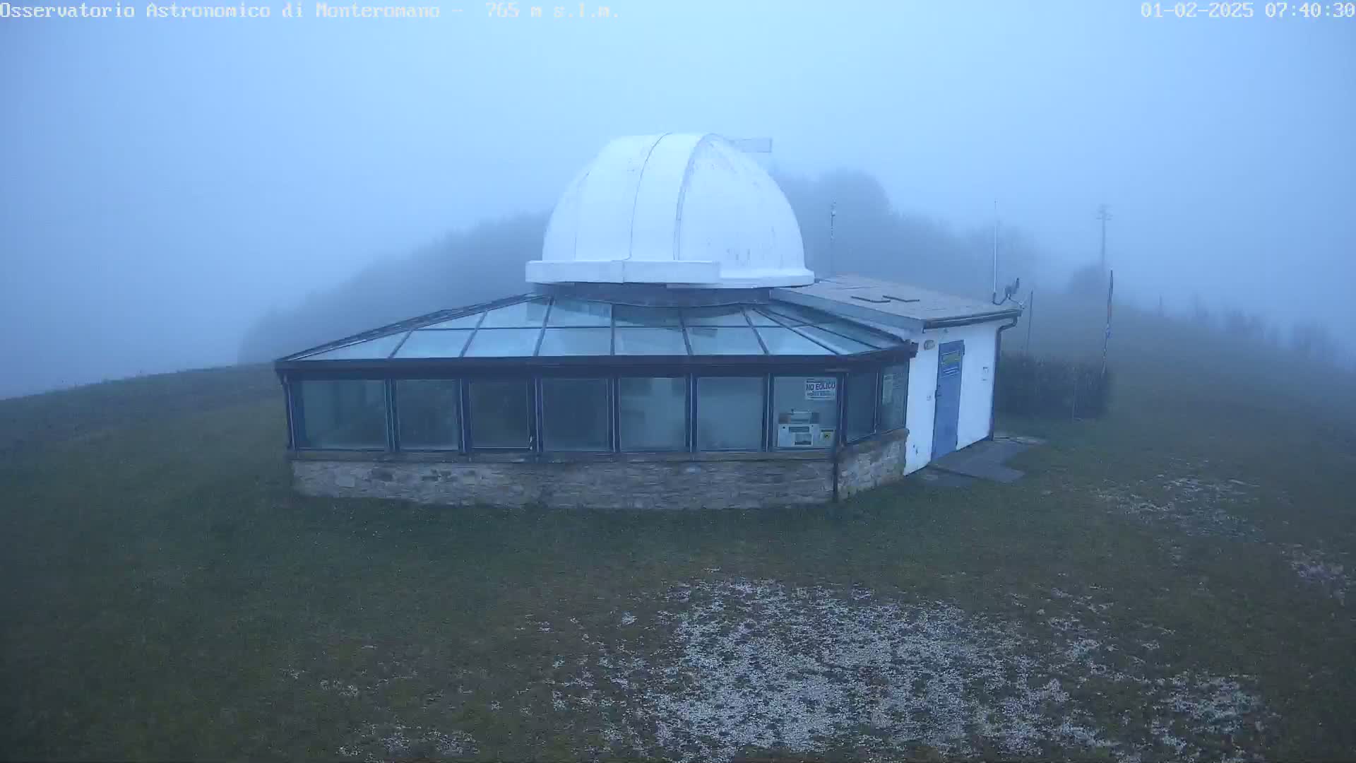 A white-domed observatory building with a glass-roofed addition sits on a grassy hill shrouded in dense fog.