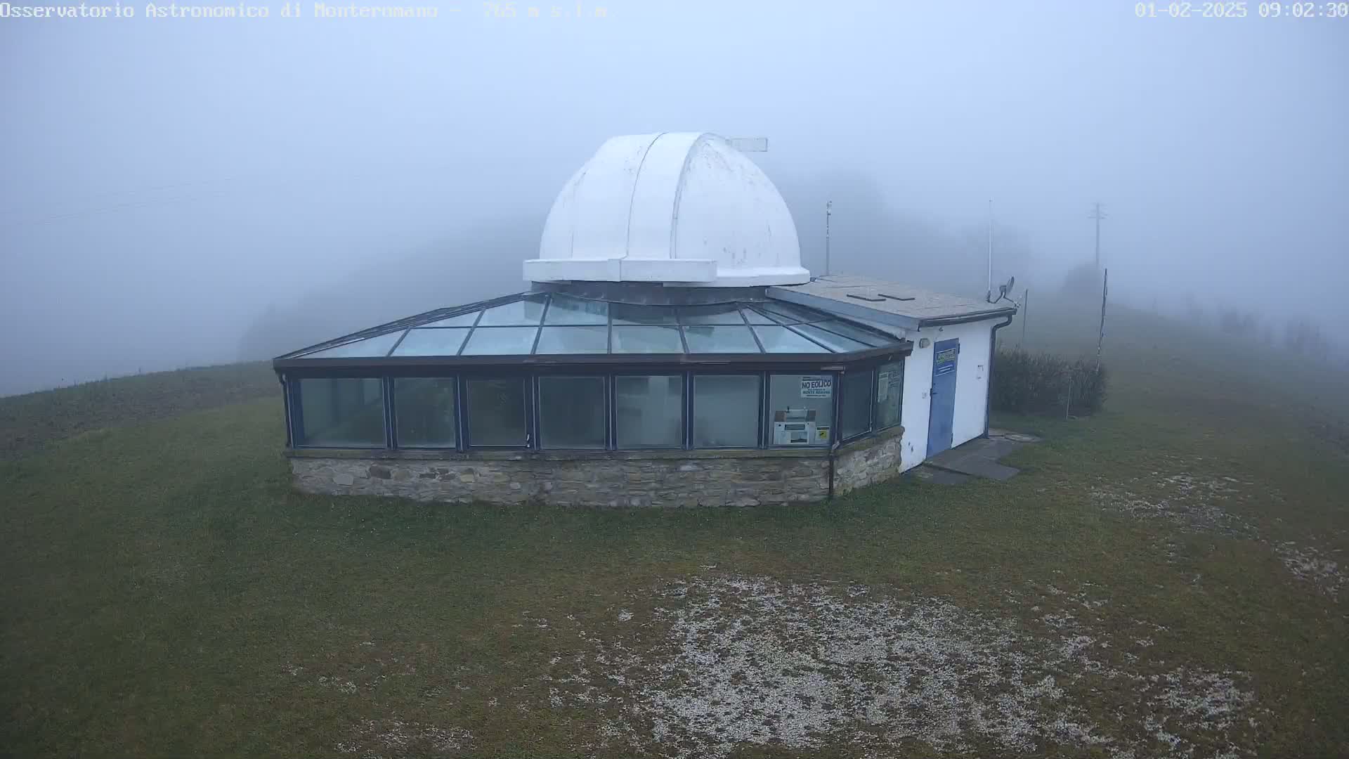 A stone building with a glass roof and a white dome sits on a grassy hill in thick fog.