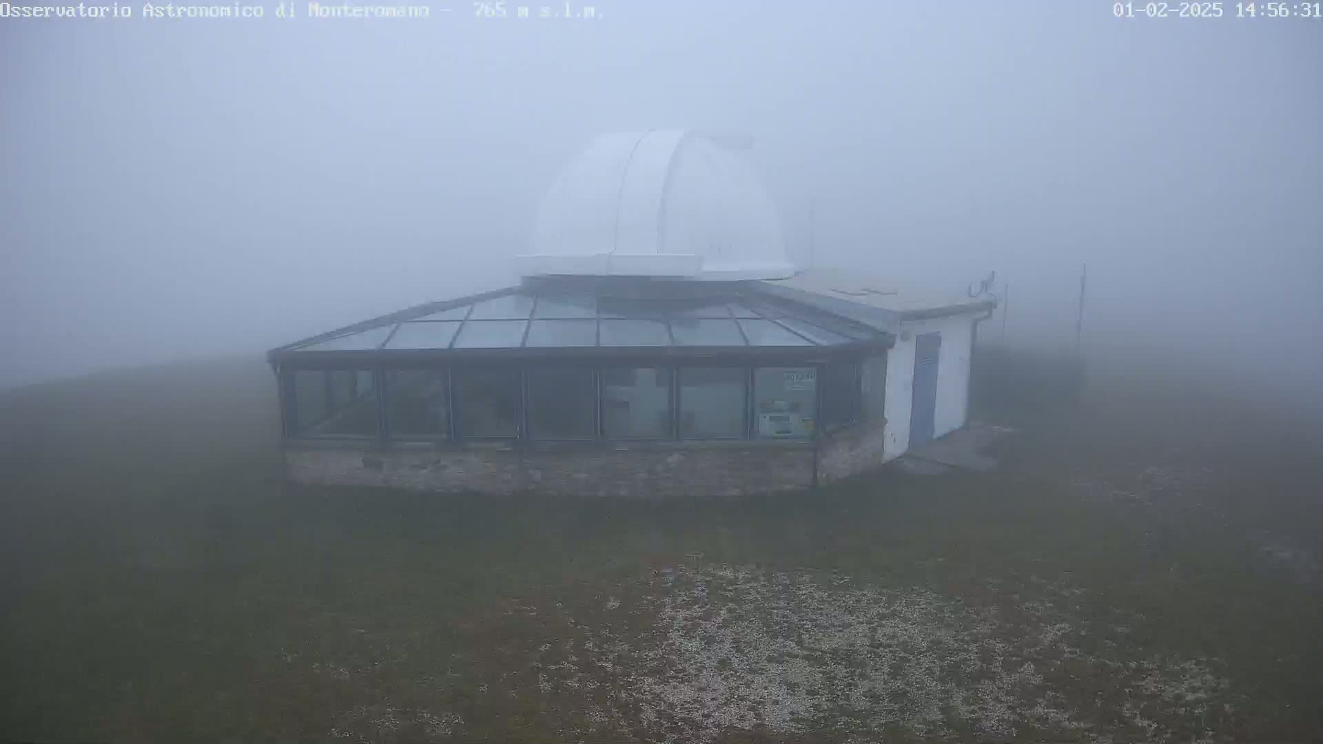 A low-lying observatory building with a glass-roofed addition and a dome is shrouded in thick fog.