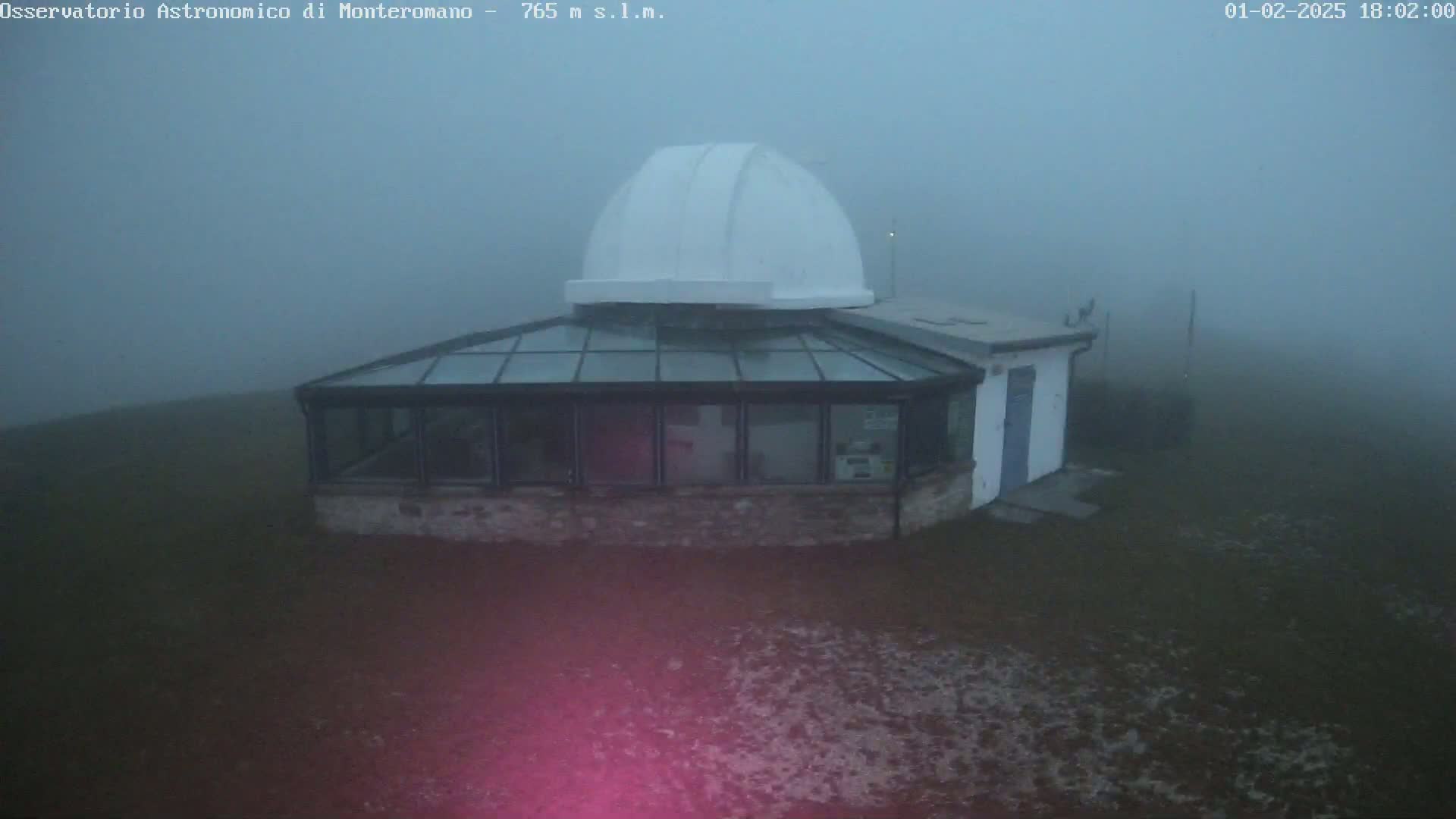 A white-domed observatory building with a glass conservatory is shrouded in thick fog.