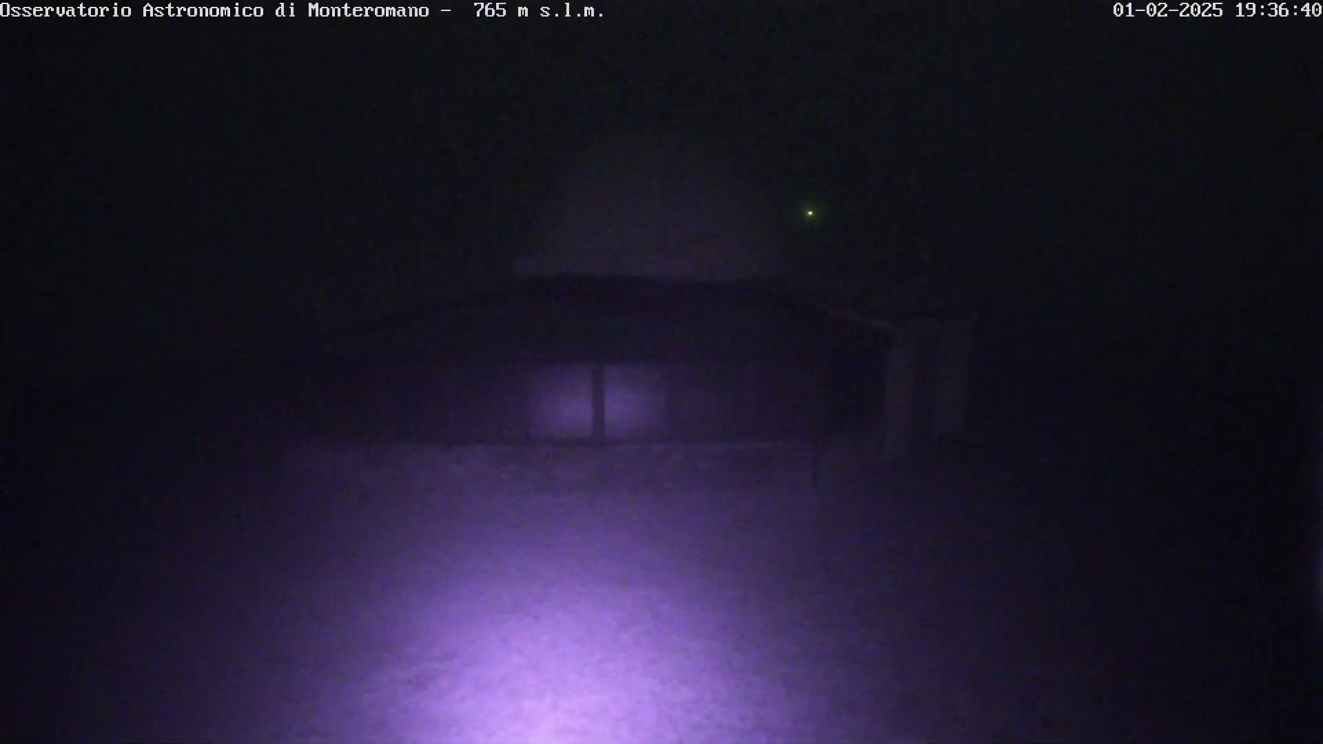 A dark building with a dome-shaped roof is seen at night in foggy or hazy conditions, illuminated by a bright light source in the foreground.
