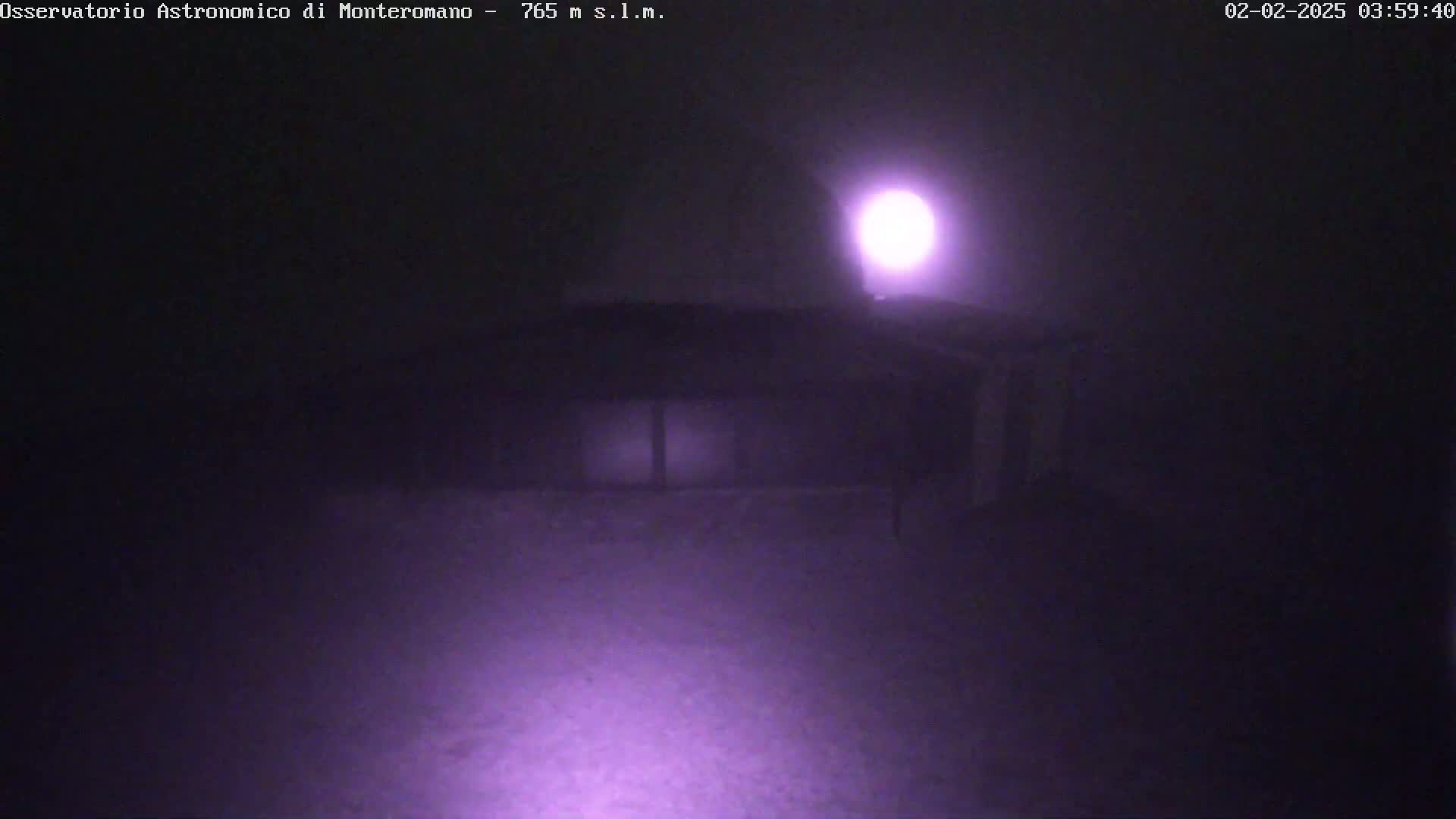 A dimly lit building is visible in the foggy night, illuminated by a bright light source above.