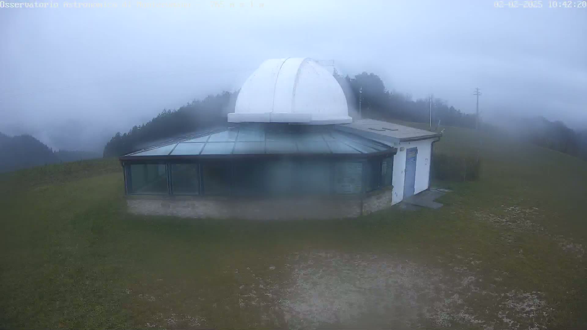 A white-domed observatory building sits on a grassy hill in foggy conditions.