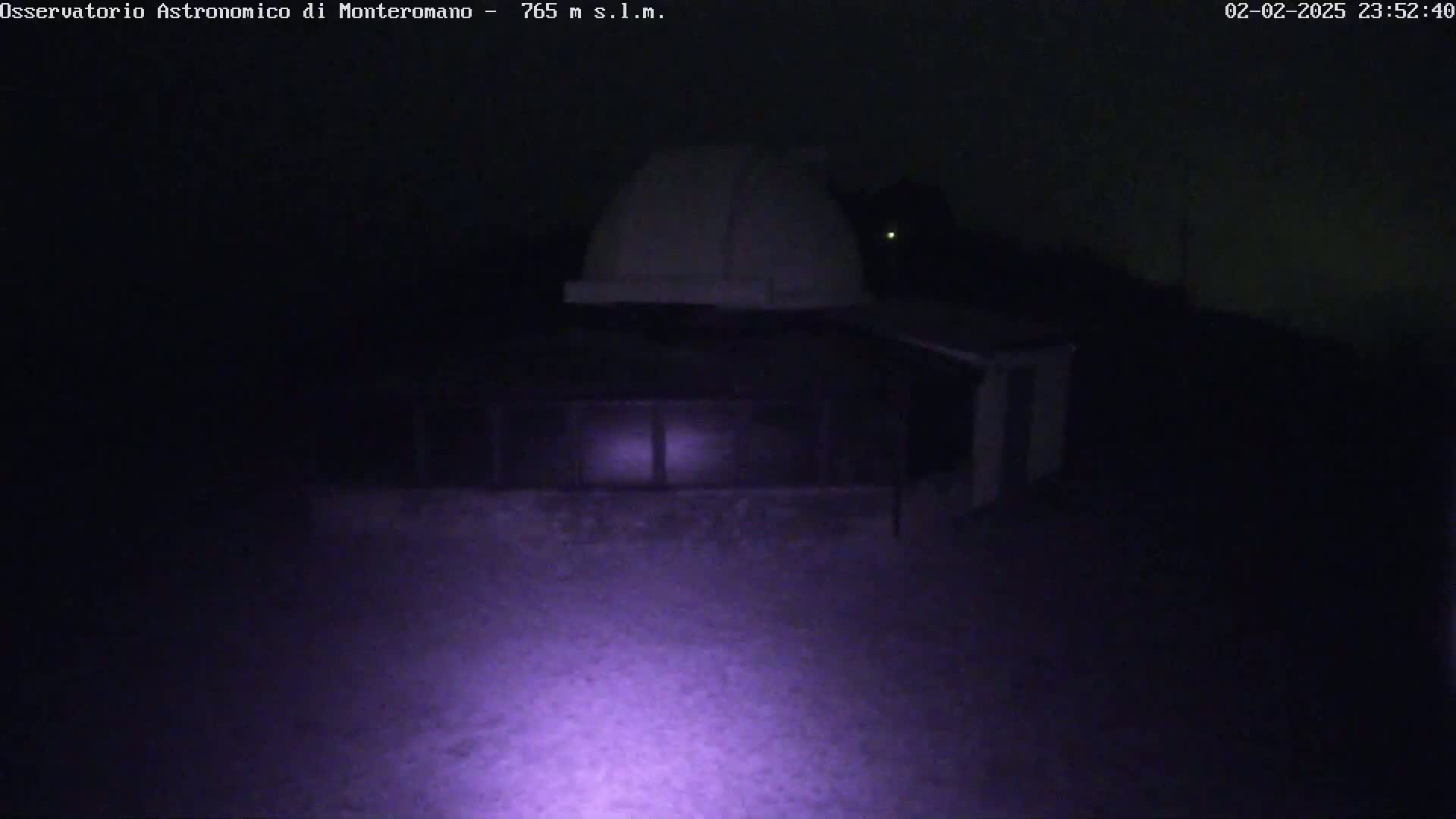 A nighttime low-light image shows a white dome-shaped observatory building with a beam of light illuminating the ground in front.