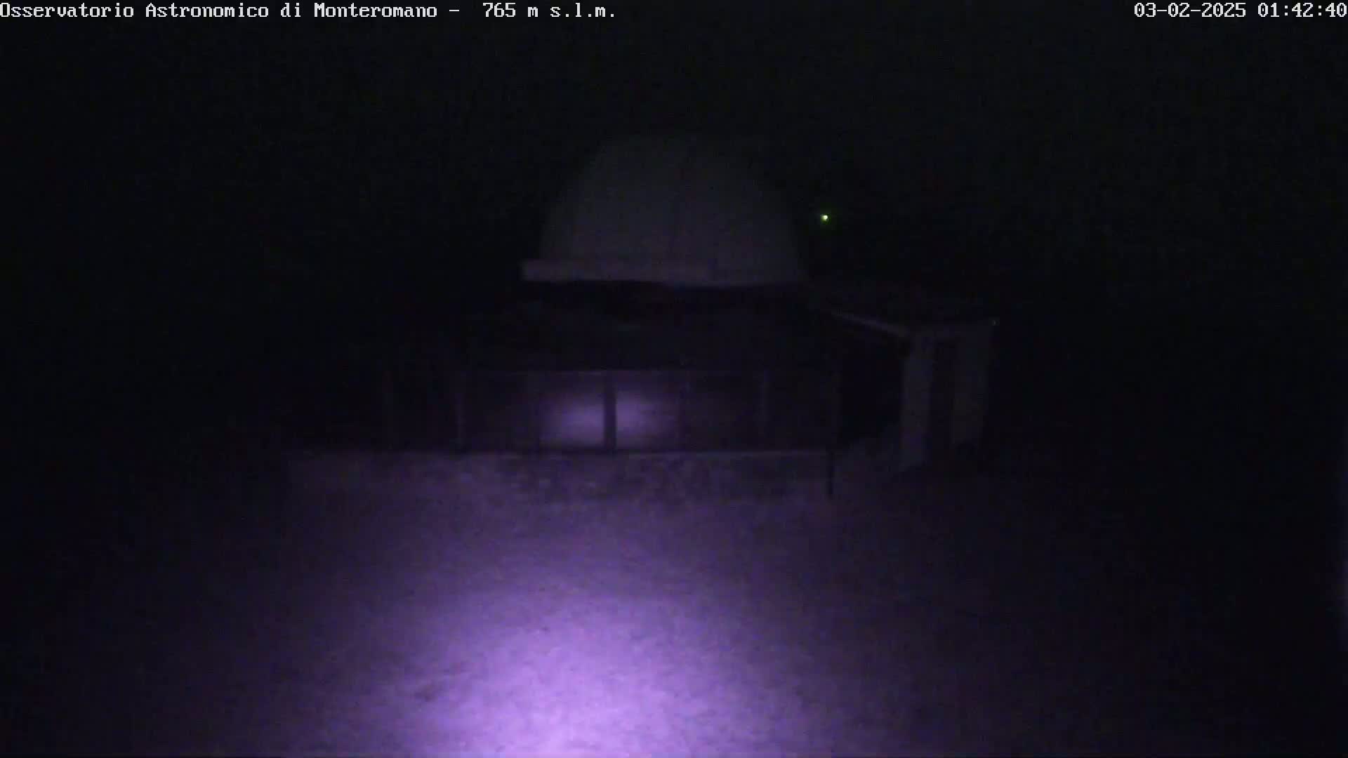 A low-light nighttime image shows a white dome-shaped structure and a rectangular building, possibly an observatory, covered in snow.