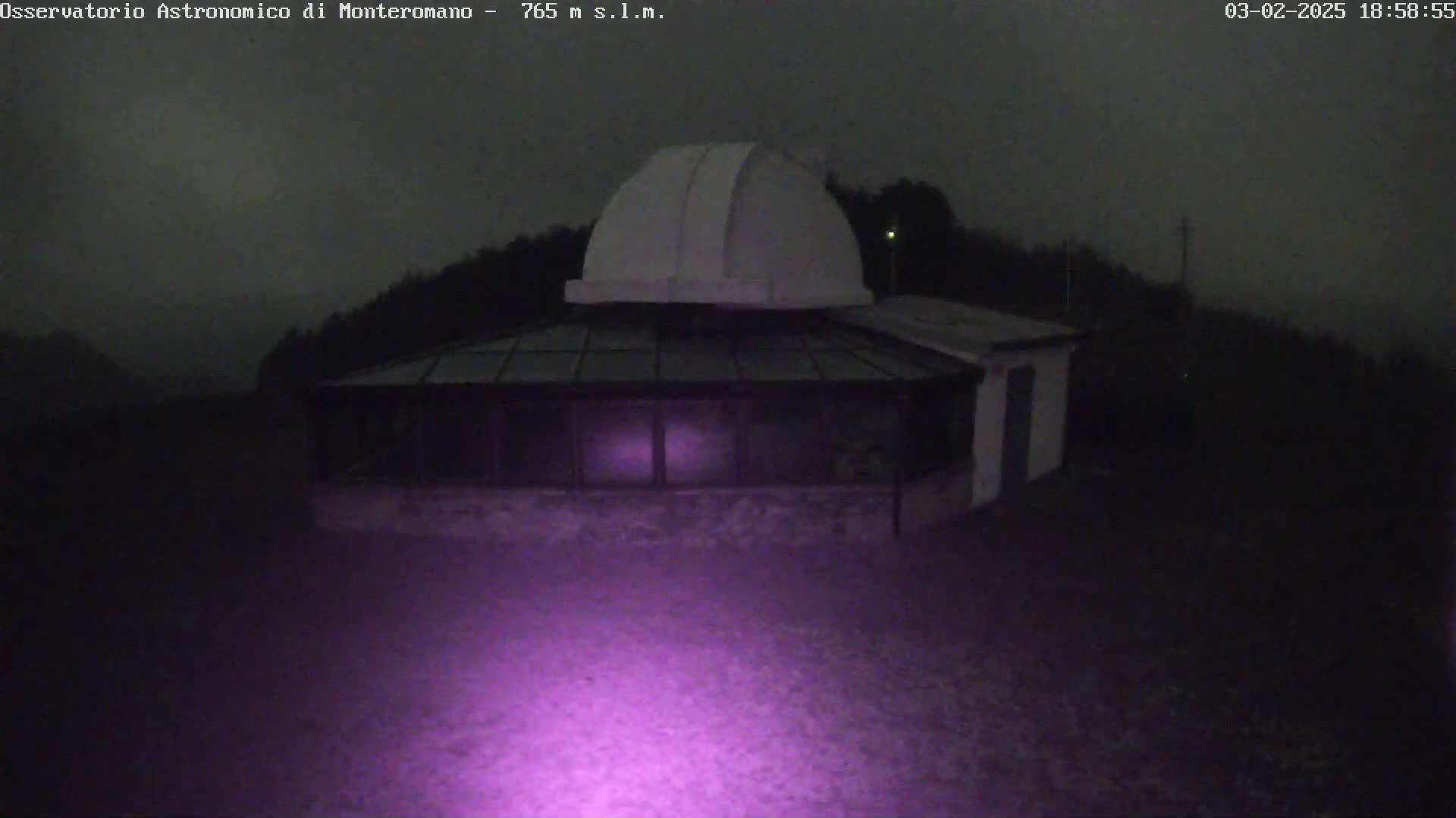 A white observatory dome sits atop a low building under a dark, overcast night sky.