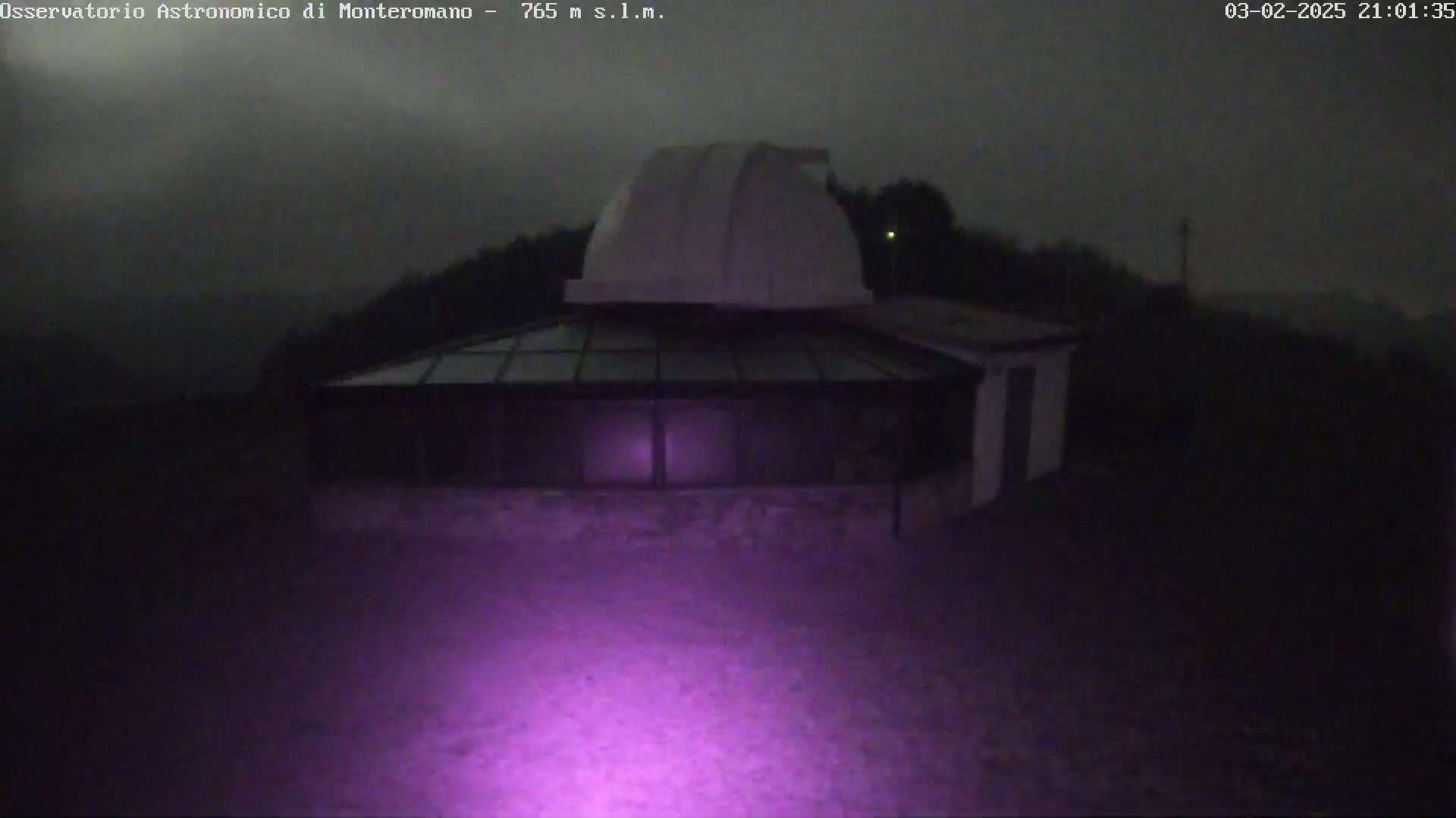 A white observatory dome sits atop a low building under a dark, overcast night sky.