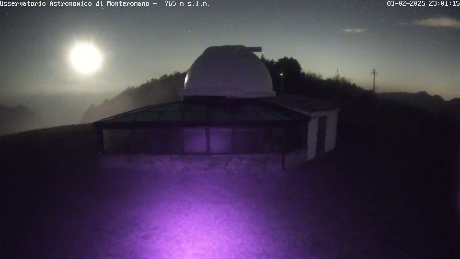A building with a dome sits atop a hill shrouded in fog under a bright moonlit night sky.