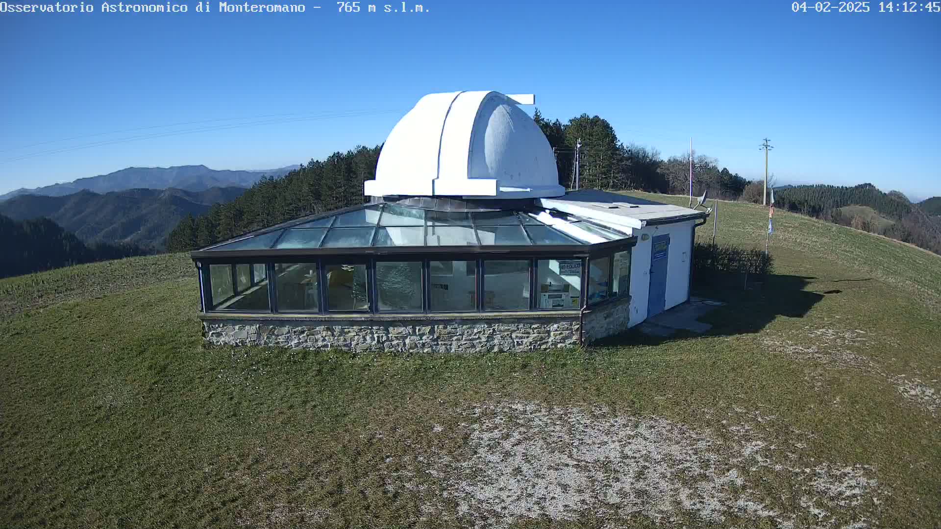 A white-domed observatory building with a glass-roofed addition sits on a grassy hilltop under a clear blue sky.