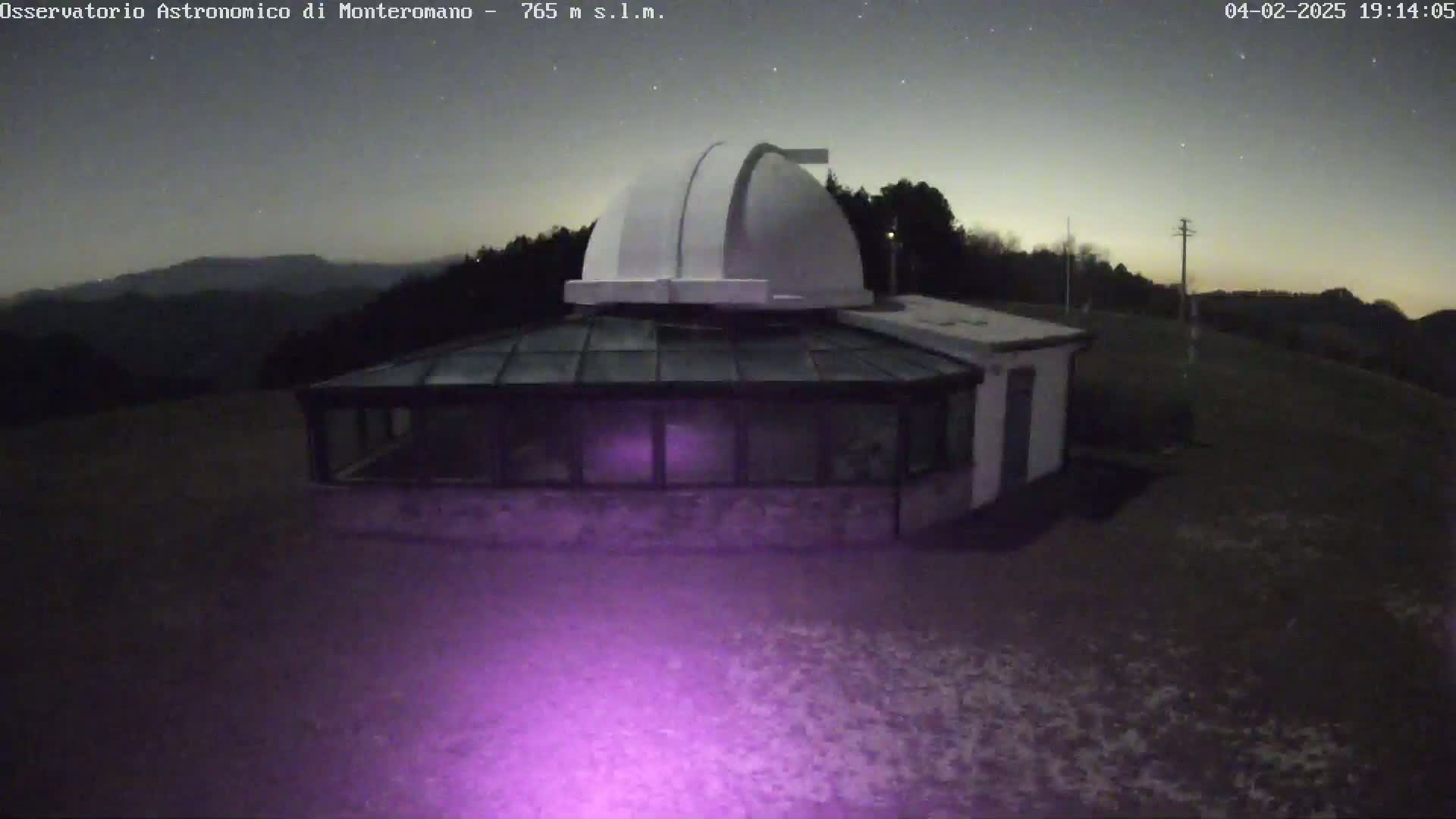 An observatory with a dome and attached glass building sits on a hill under a mostly clear night sky.