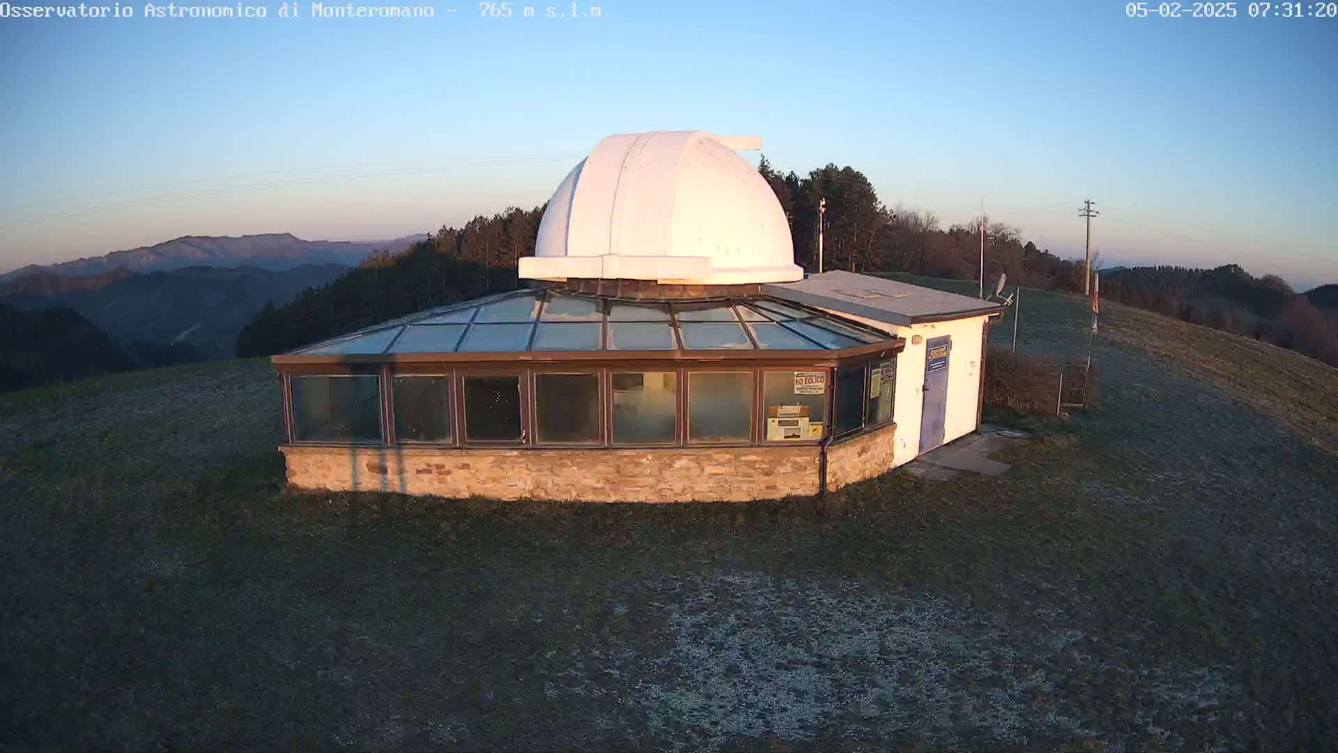 A stone observatory building with a white dome sits atop a hill at sunrise, overlooking a mountainous landscape.