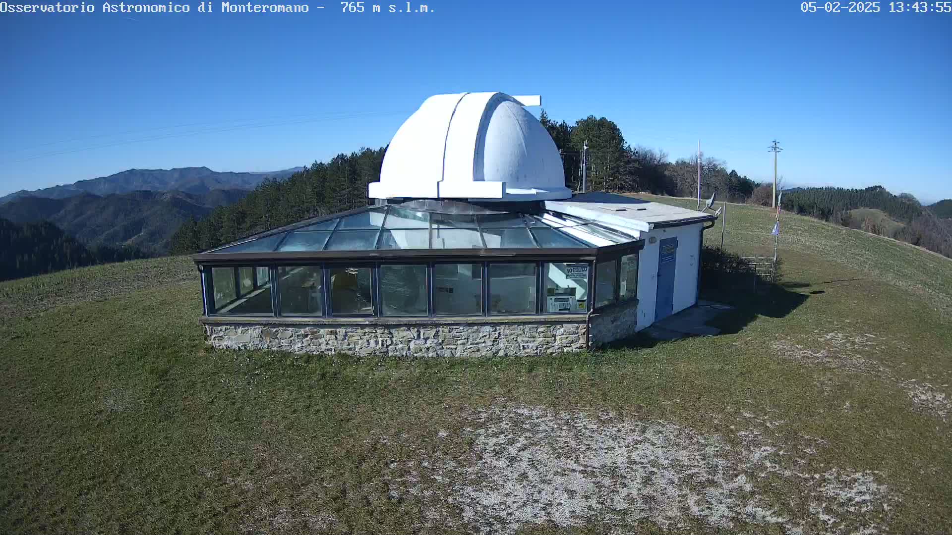 A small stone observatory with a glass-roofed addition and a white dome sits on a grassy hilltop under a clear blue sky.