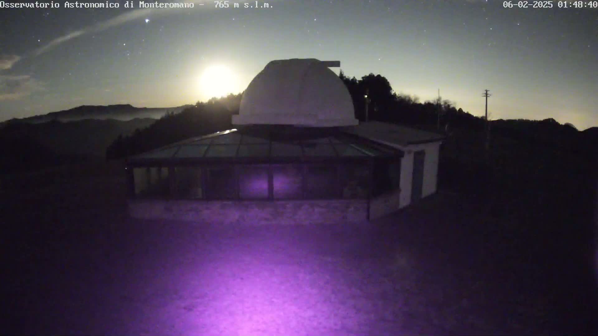 Under a nighttime sky with a bright moon and stars, a white observatory dome sits atop a building with a glass-roofed addition.