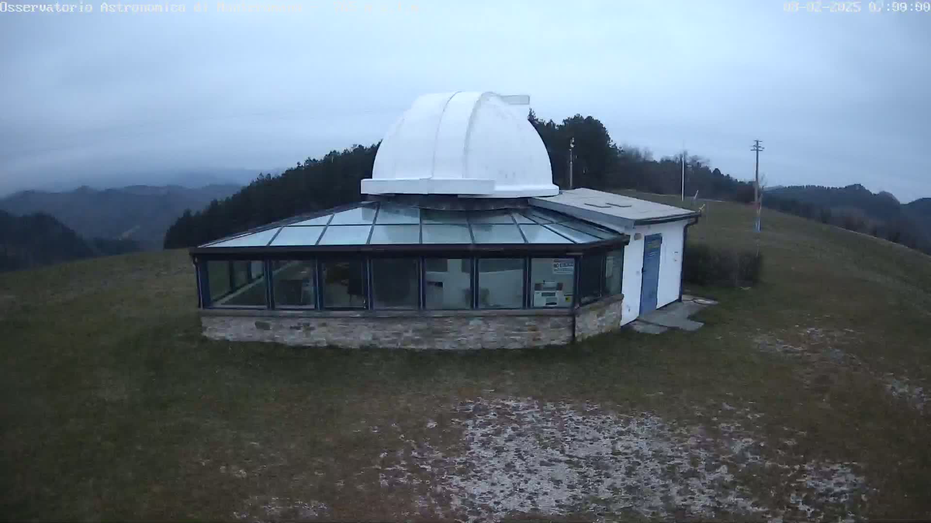 A stone building with a glass roof and a white dome sits atop a hill on an overcast day, overlooking a range of distant hills.