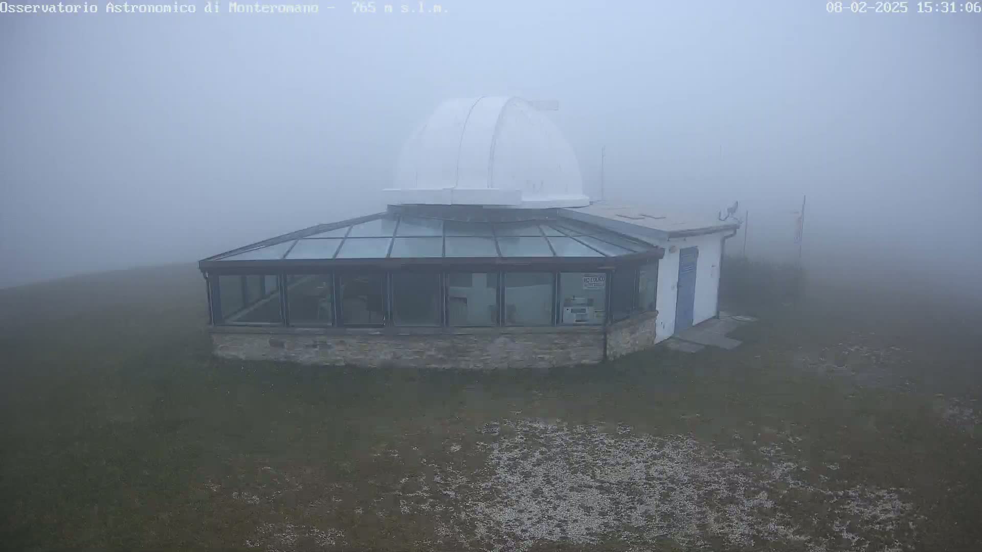 A white-domed observatory building with a glass-roofed addition sits shrouded in dense fog on a flat, grassy expanse.
