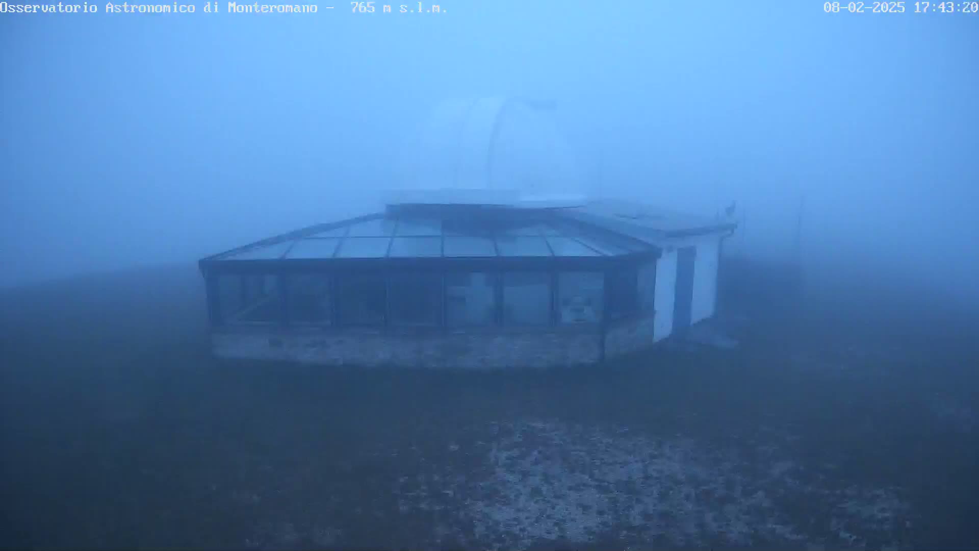 A building with a glass roof and a dome-shaped structure is shrouded in thick fog.