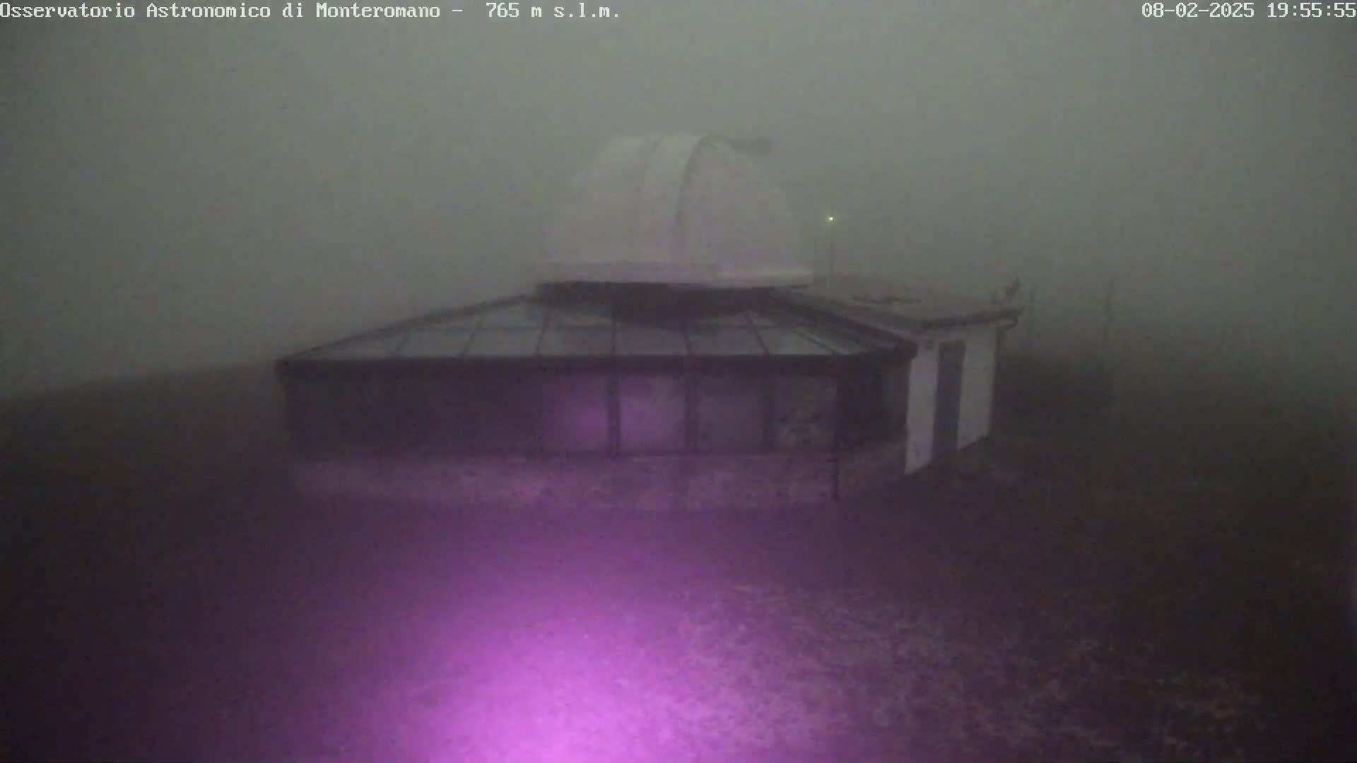 A building with a dome and glass roof is shrouded in thick fog.