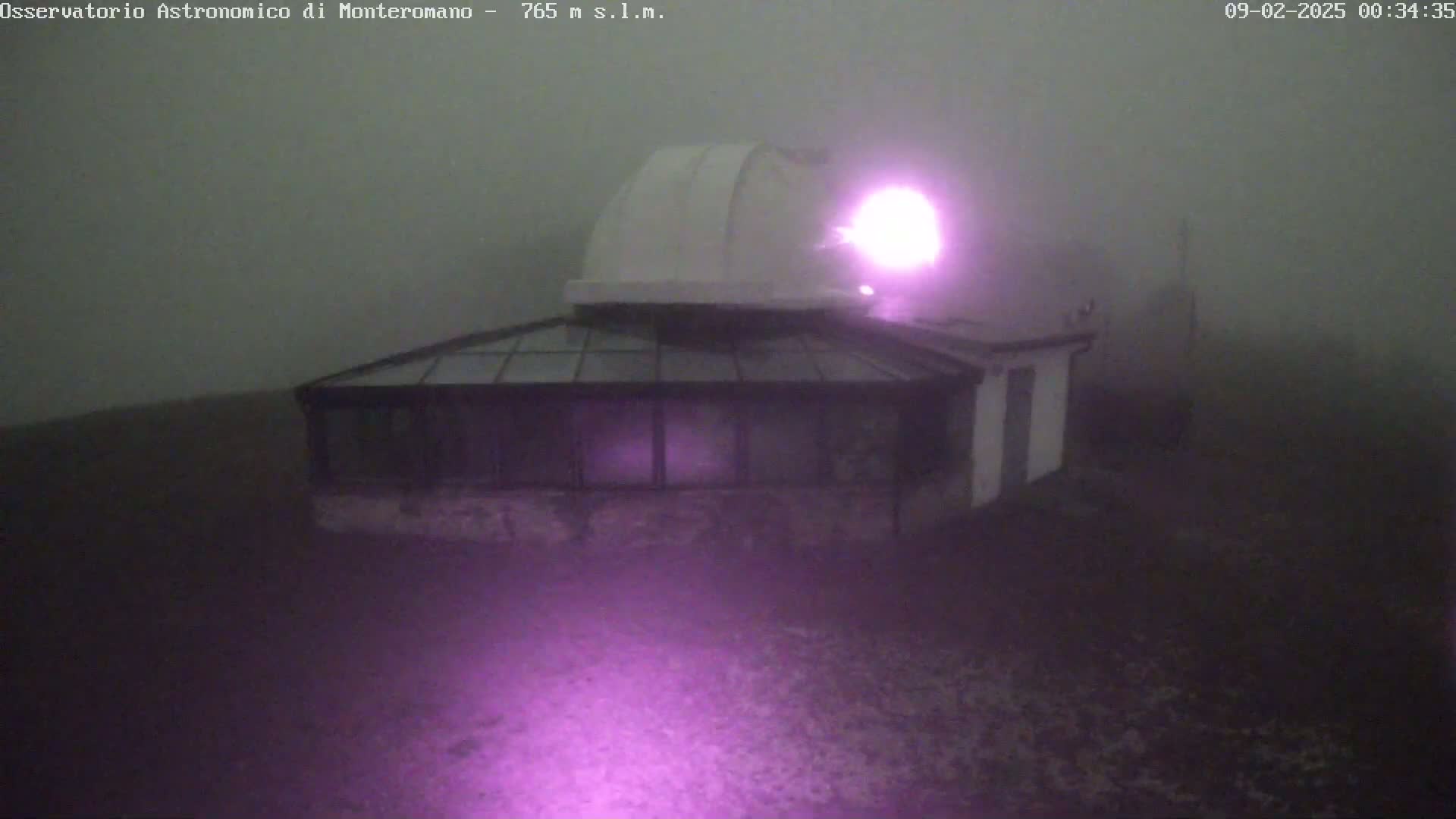 A white observatory building with a dome is shrouded in thick fog, illuminated by a purple light.