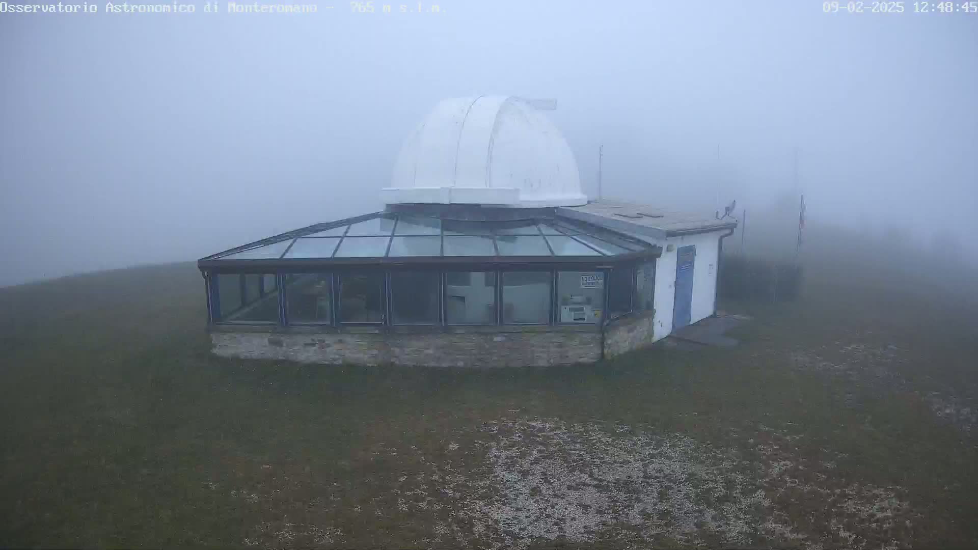 A white-domed observatory building with a glass-roofed addition is shrouded in dense fog.