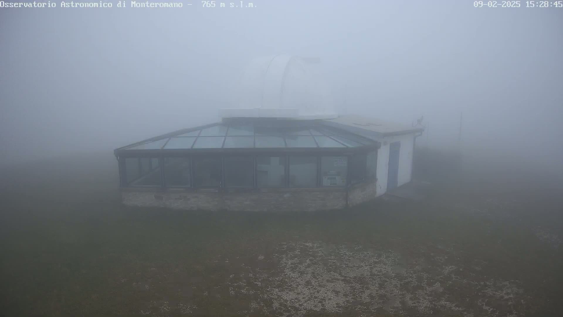 A stone building with a glass roof and a dome-shaped structure attached is shrouded in thick fog.