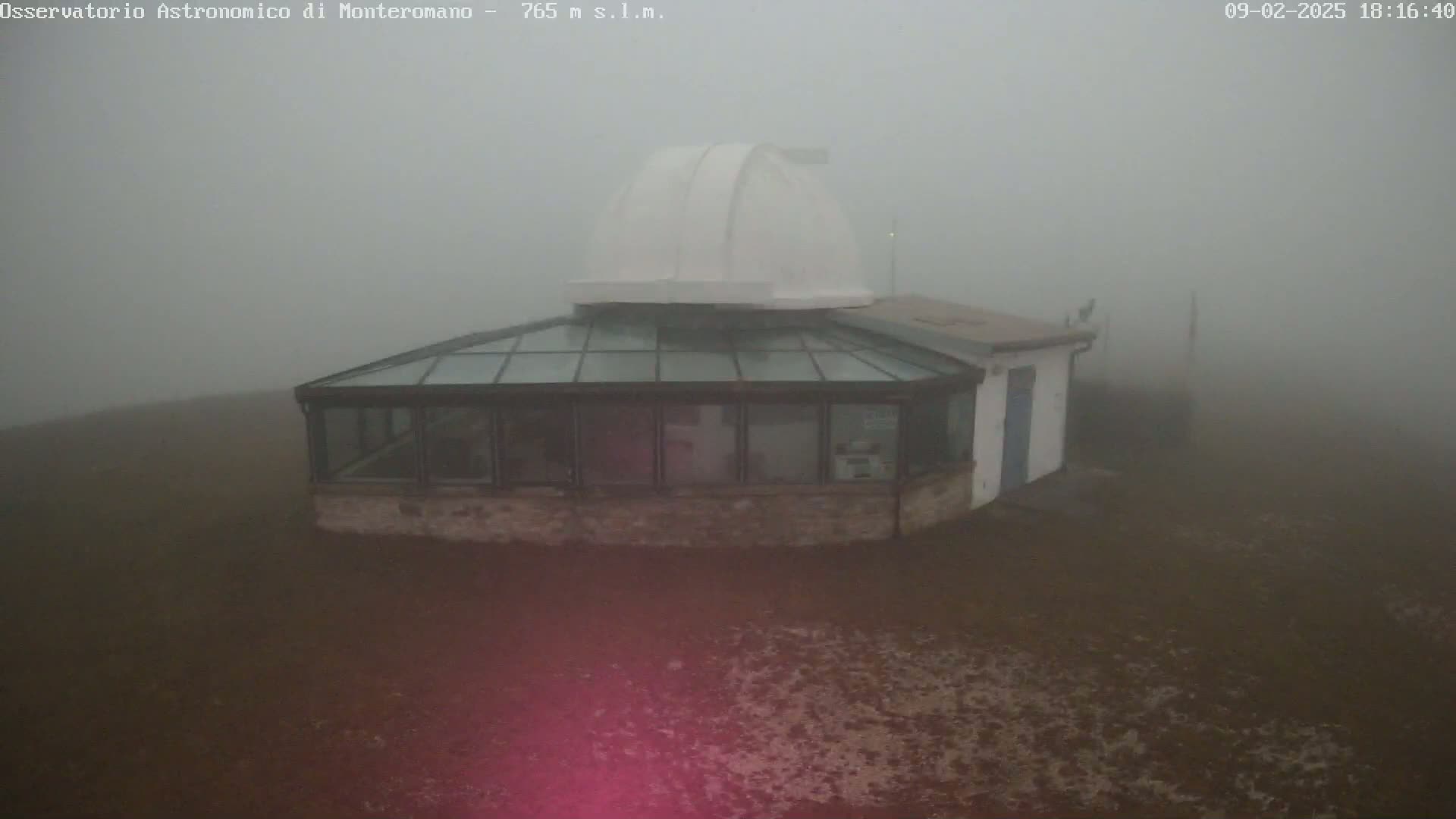 A small observatory building with a glass addition and a white dome sits on a fog-covered, brown expanse of land.