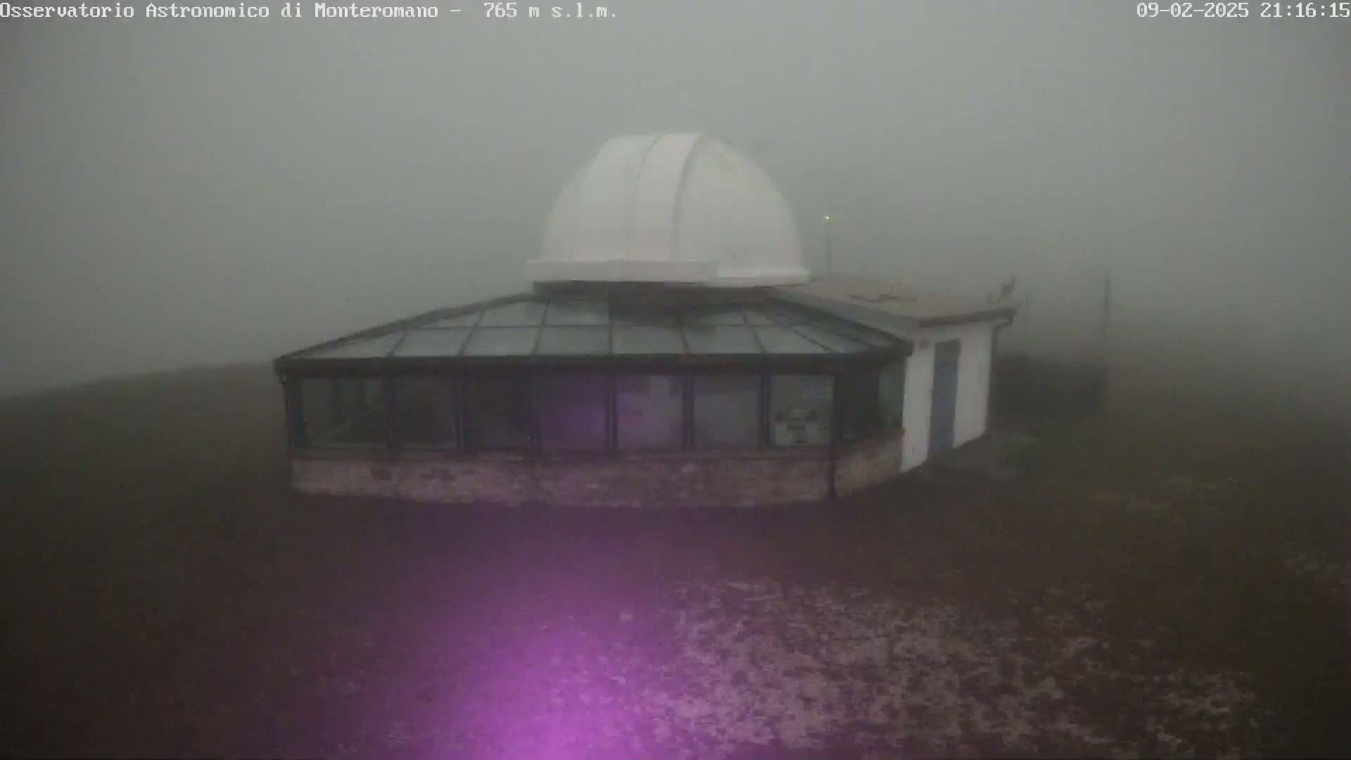 A white dome-shaped building with a glass-roofed addition sits on a foggy, dark-colored ground.
