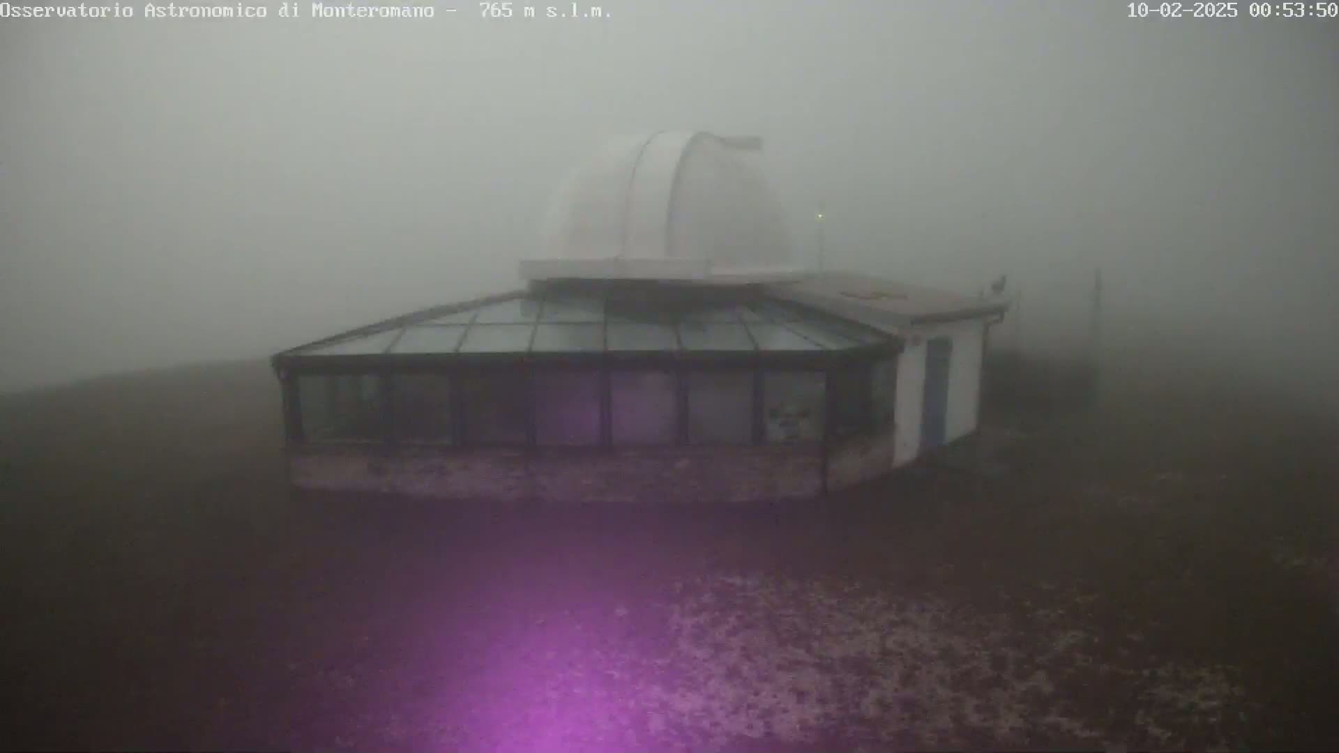 A white observatory dome and attached glass-roofed building are shrouded in thick fog.