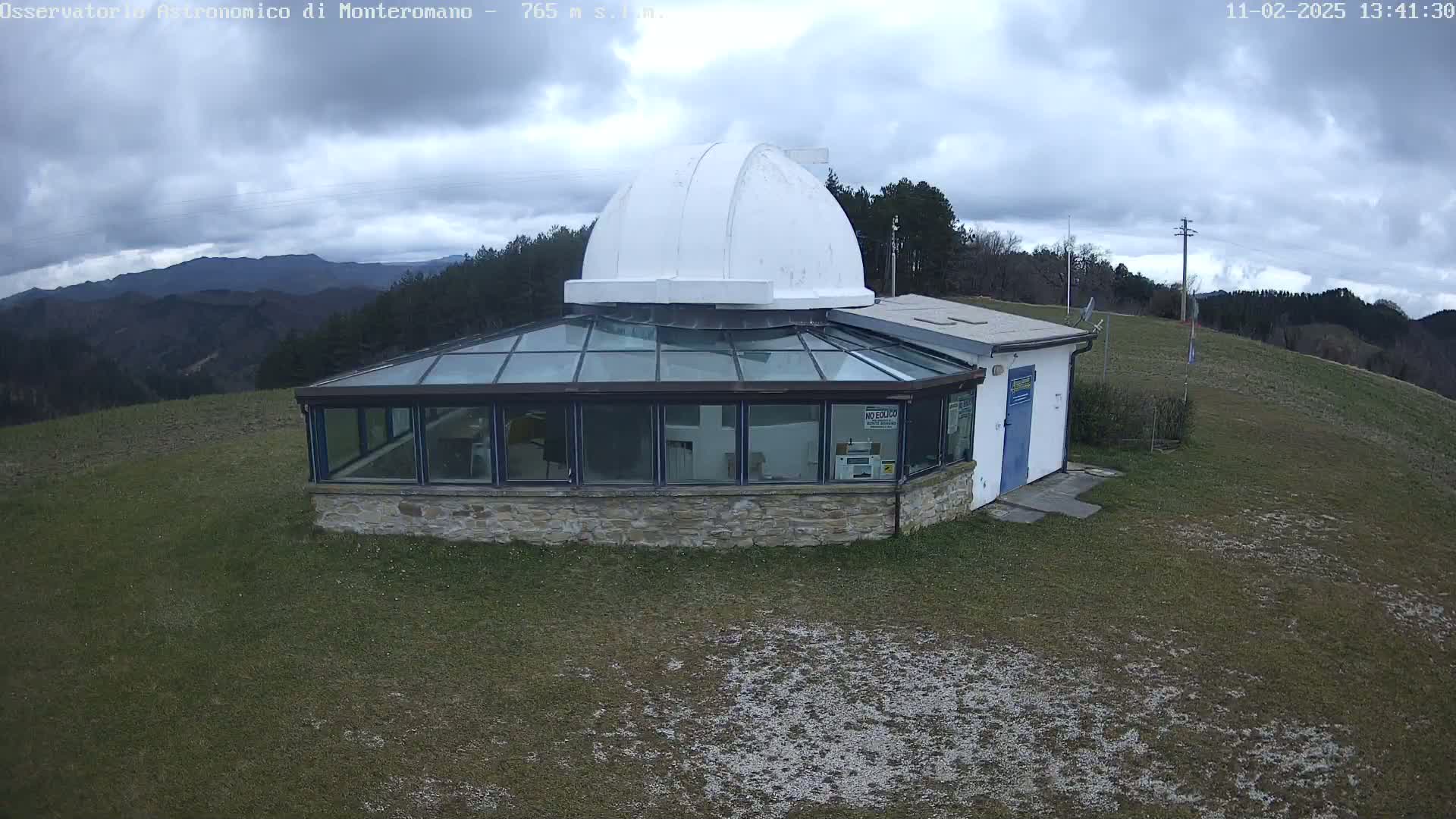 A stone building with a glass enclosure and a white dome sits on a grassy hilltop under a cloudy sky.