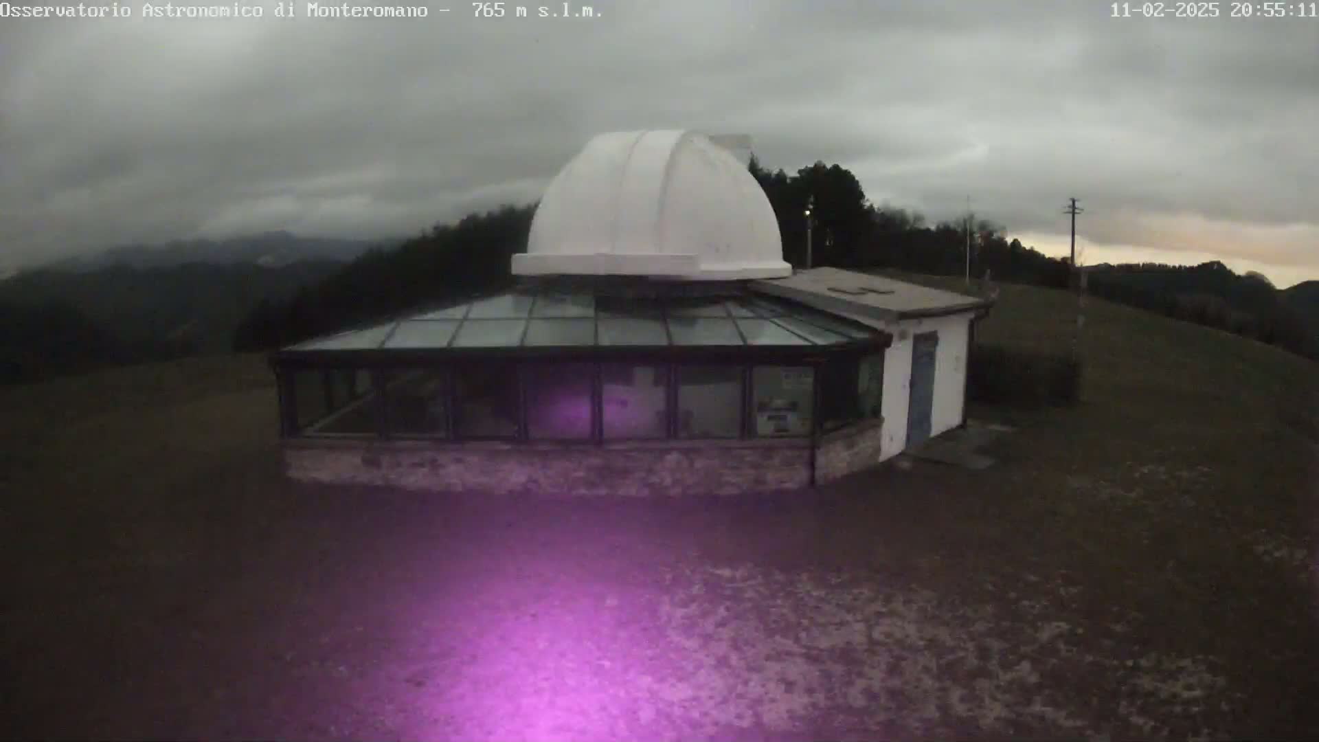 A white dome observatory sits atop a stone building with a glass conservatory under an overcast sky.