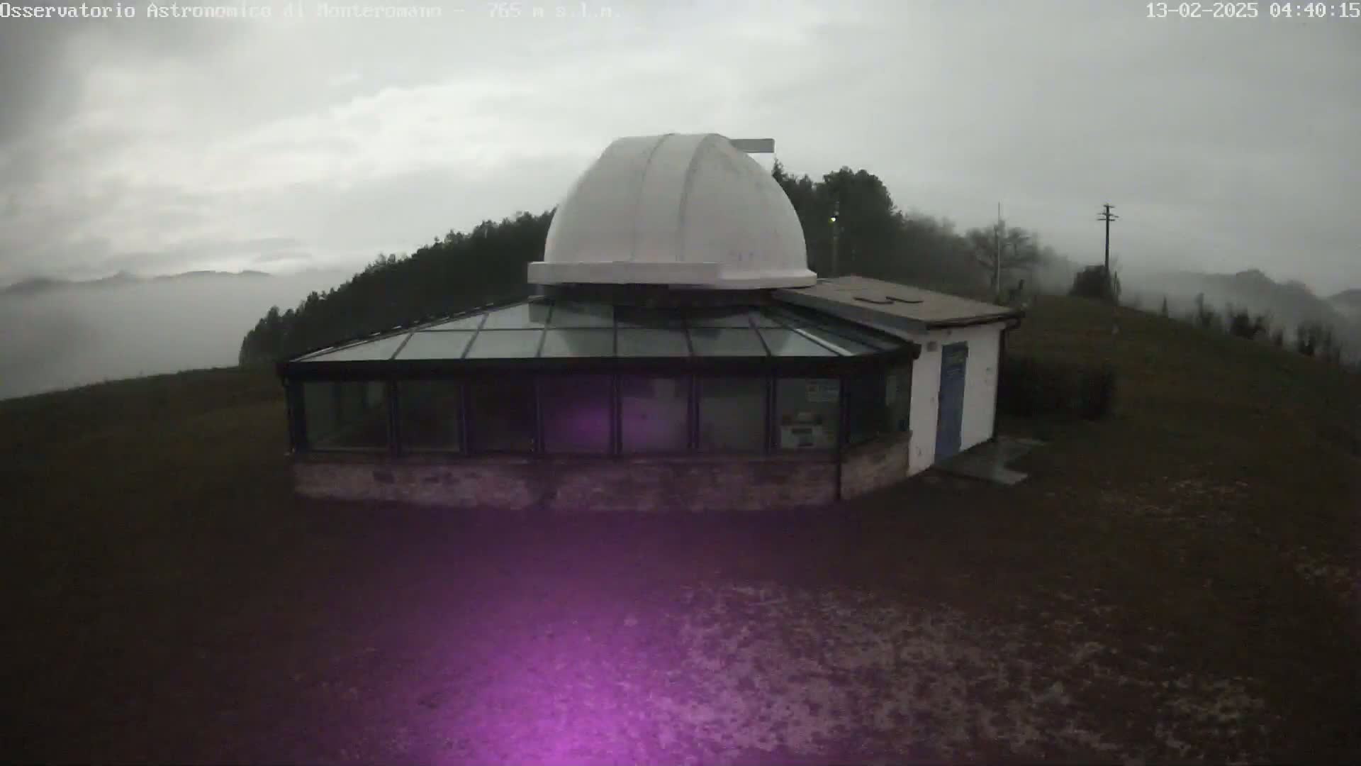 A white-domed observatory building with a glass-roofed addition sits on a hill shrouded in fog under an overcast sky.