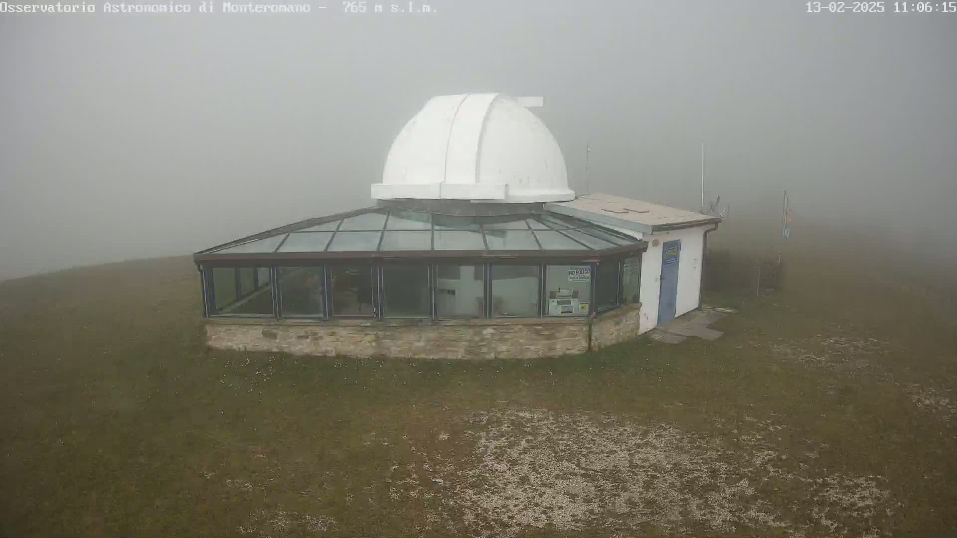 A low-lying observatory building with a white dome sits in dense fog on a grassy field.