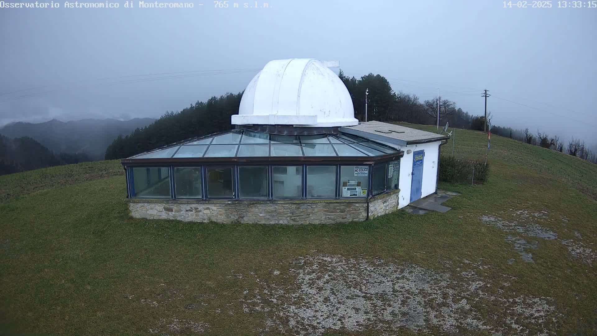 A small observatory with a white dome sits atop a grassy hill on an overcast day.