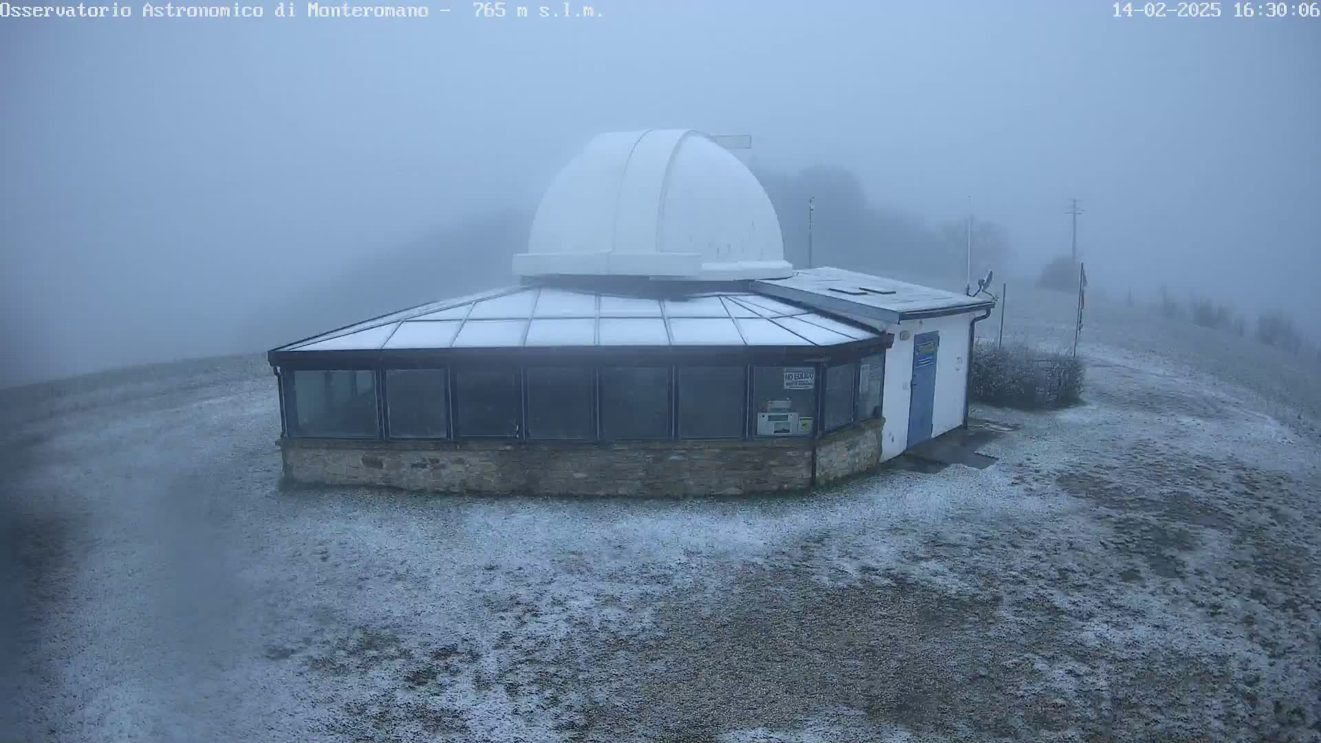 A snow-covered observatory building with a dome sits in a foggy landscape.