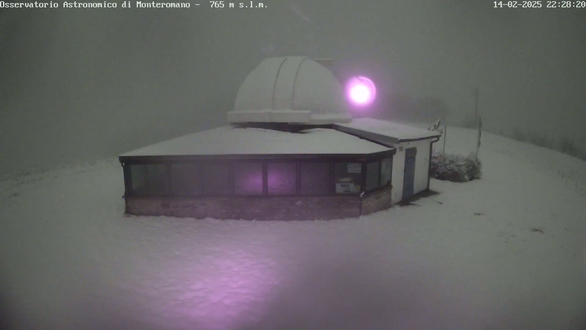 A snow-covered observatory building with a dome is visible in foggy nighttime conditions.
