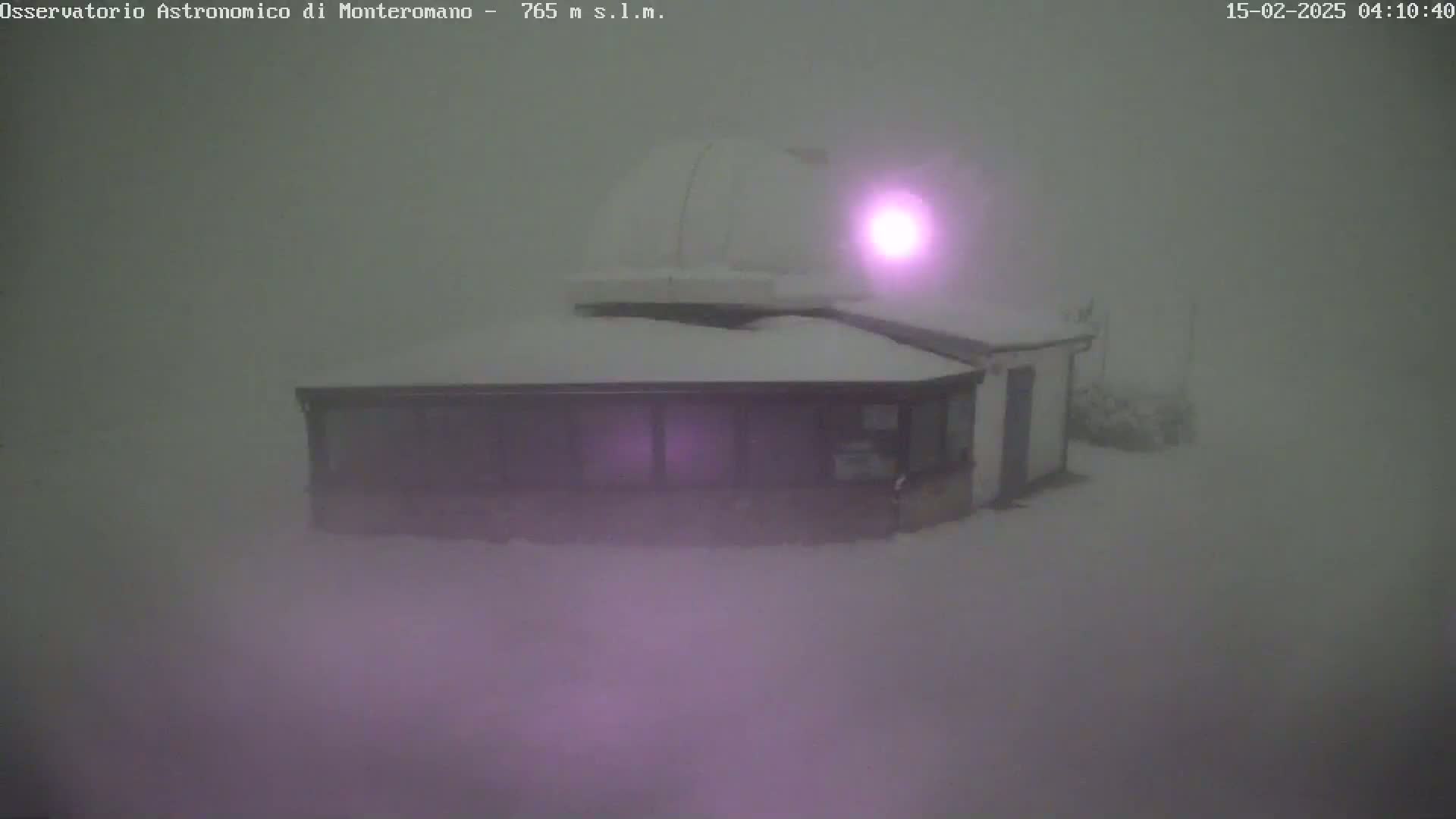 A snow-covered building with a dome on top is seen in heavy fog.