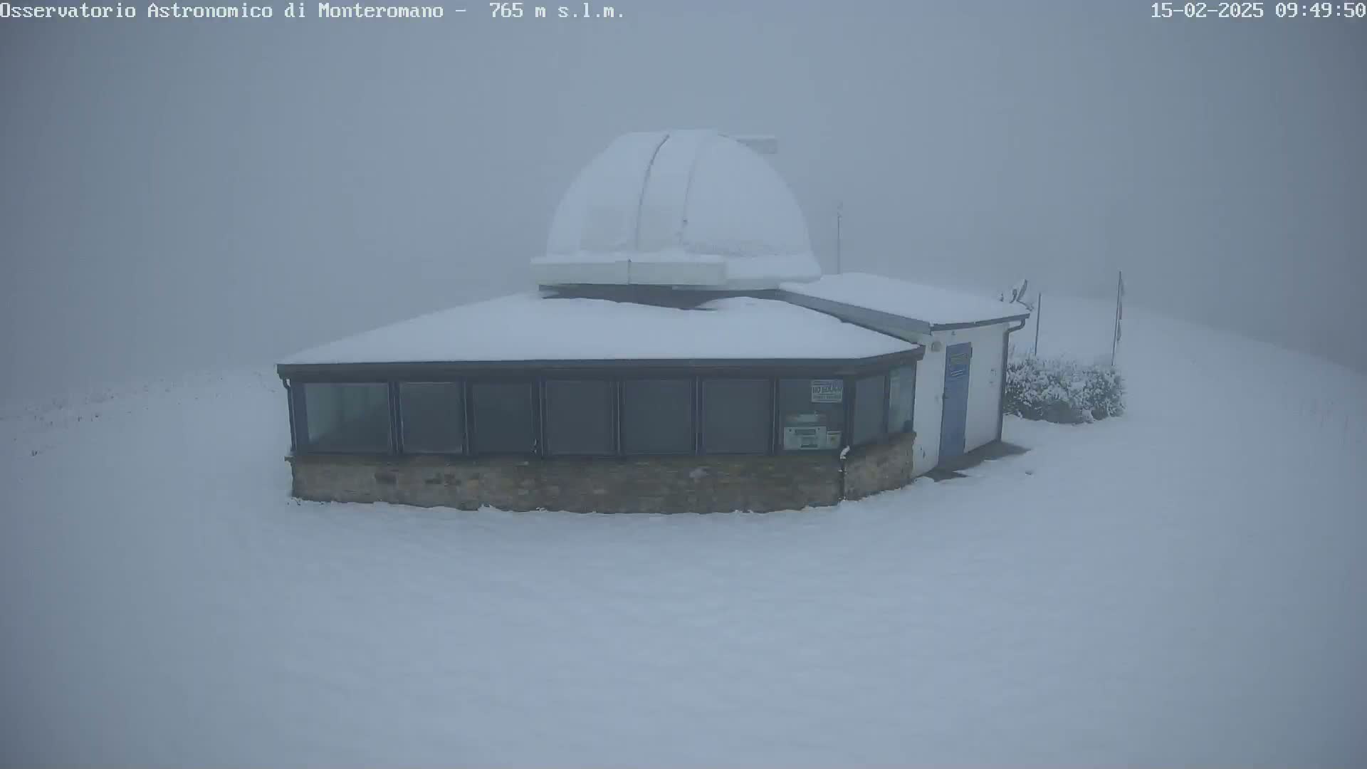 A snow-covered building with a dome-shaped structure attached sits in a foggy, snowy landscape.