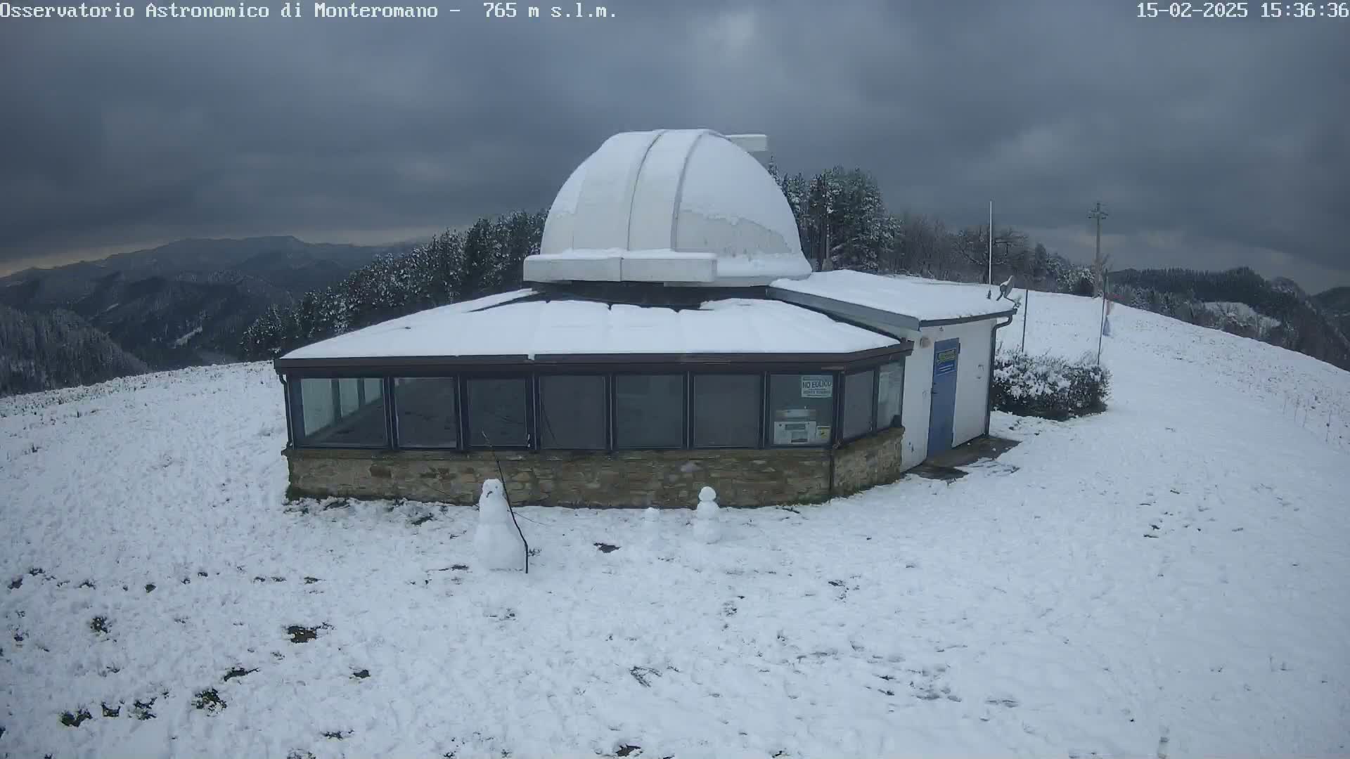 A snow-covered observatory building with a dome sits on a hilltop under an overcast sky.