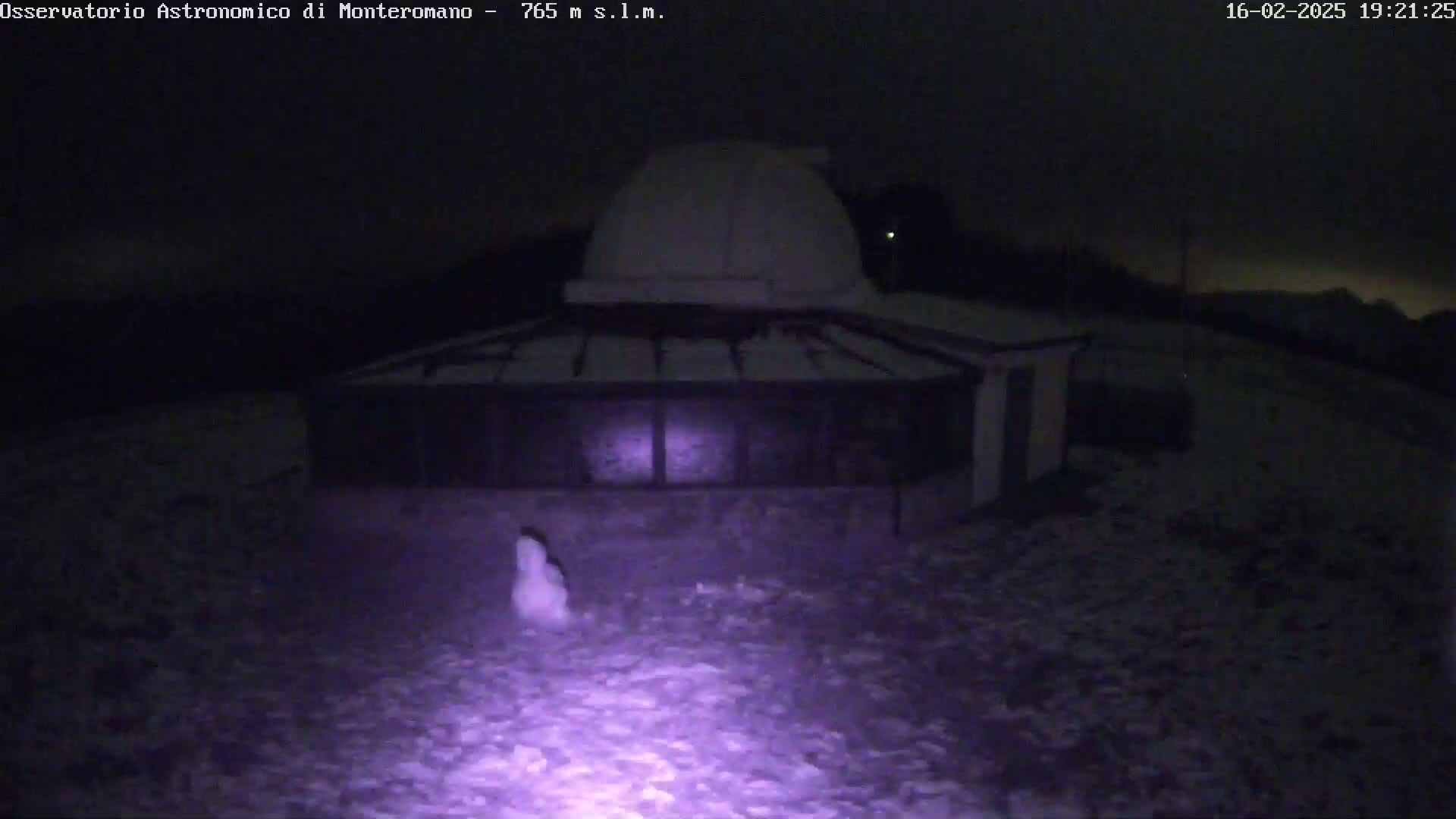 A snow-covered observatory building with a dome is illuminated at night.