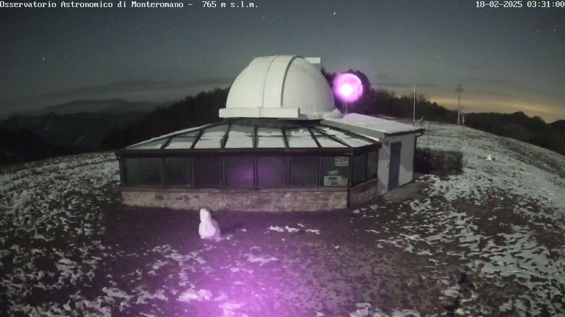 A white observatory dome sits atop a snow-covered building under a mostly clear night sky.