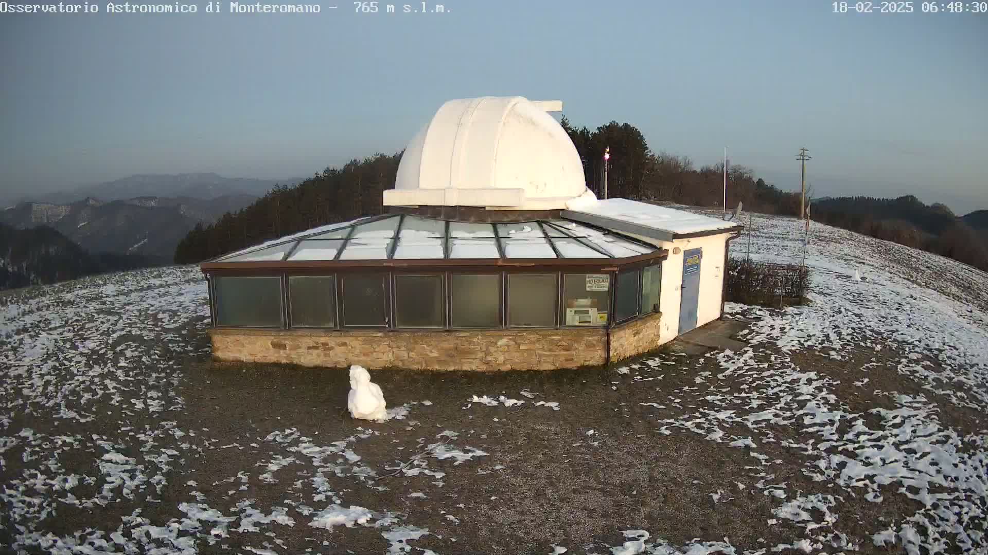 A small observatory with a white dome sits on a snow-covered hill overlooking a mountain range under a clear, twilight sky.