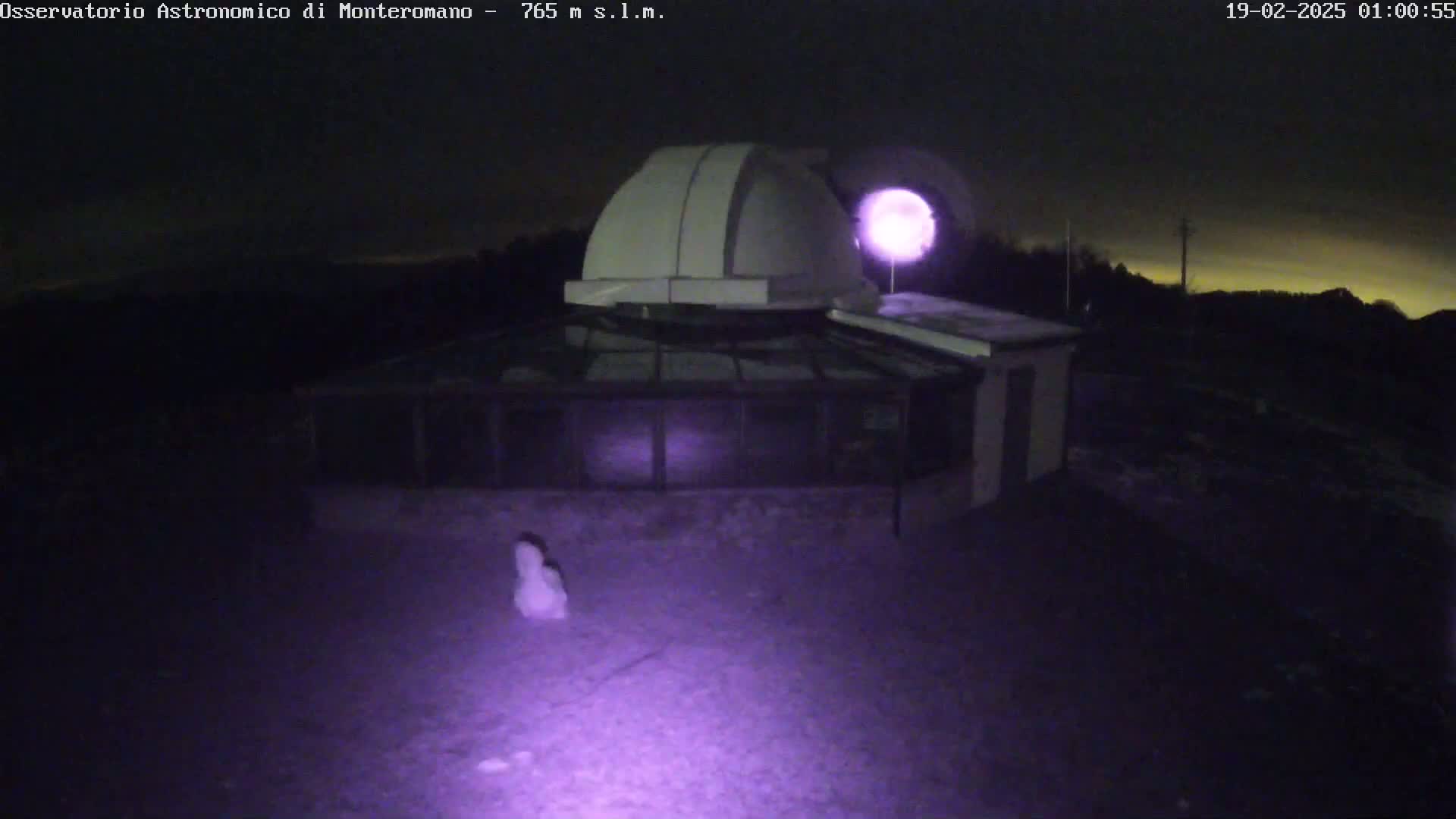 An observatory with a dome is illuminated at night under a dark, possibly cloudy sky.