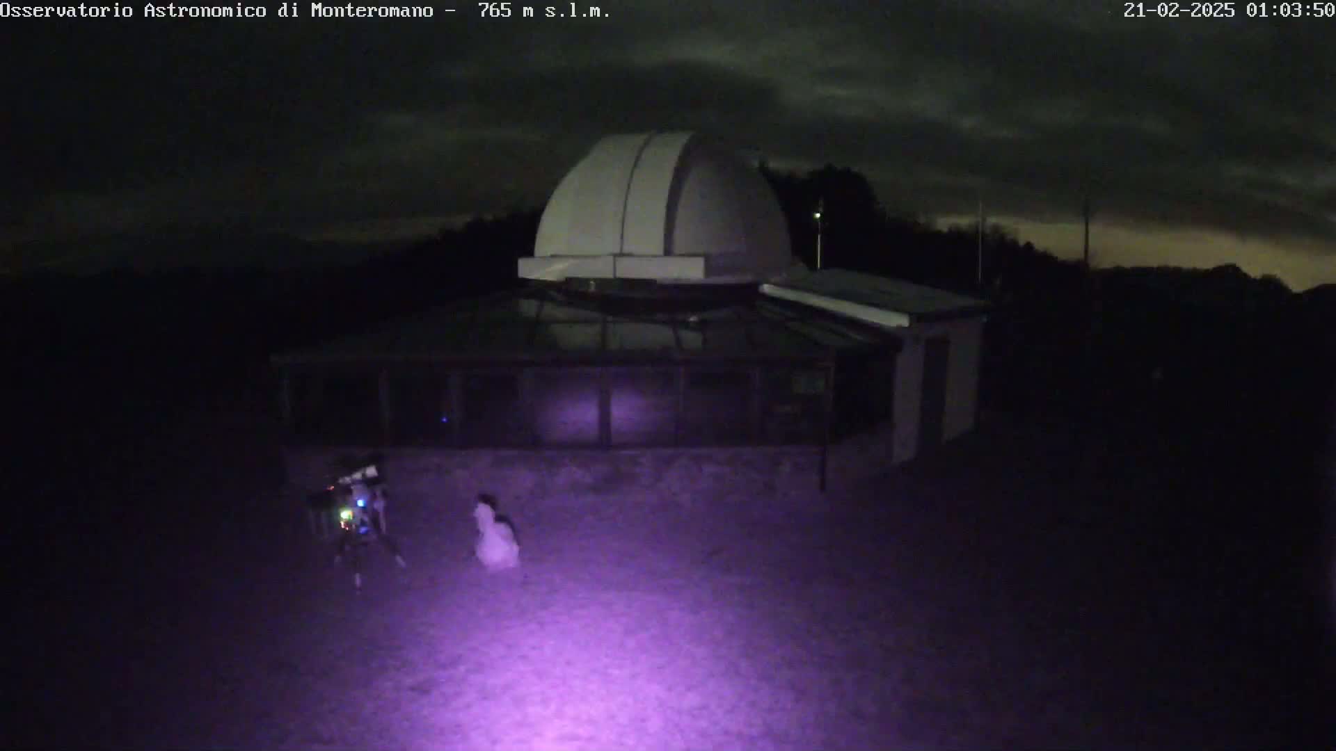An observatory with a dome is illuminated under a dark, cloudy night sky.