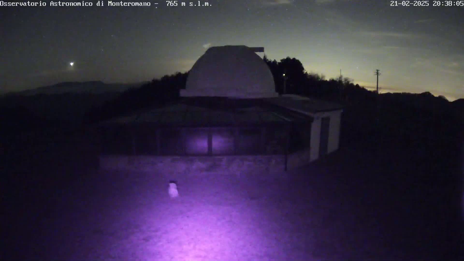 A low-light image shows a building with a dome on top, under a partly cloudy night sky.
