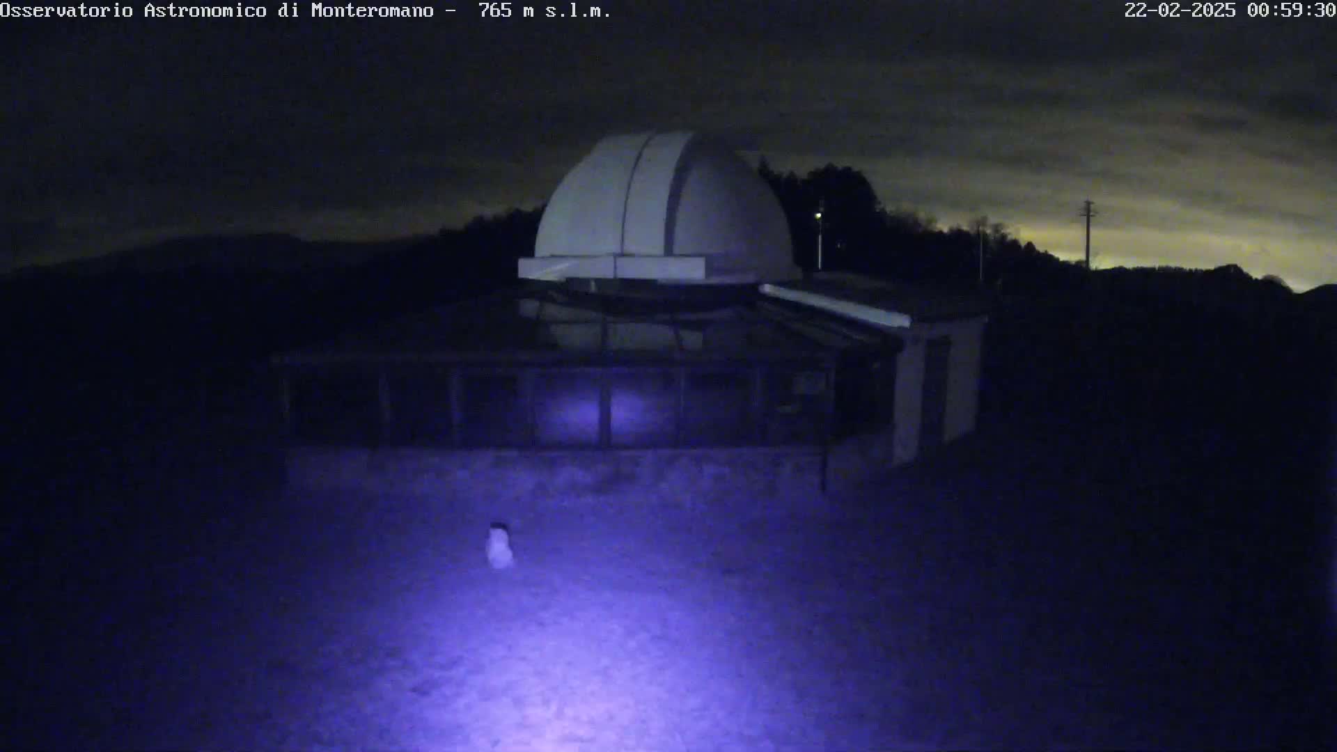 A nighttime image shows a low-lying building with a dome on top, under a cloudy sky.