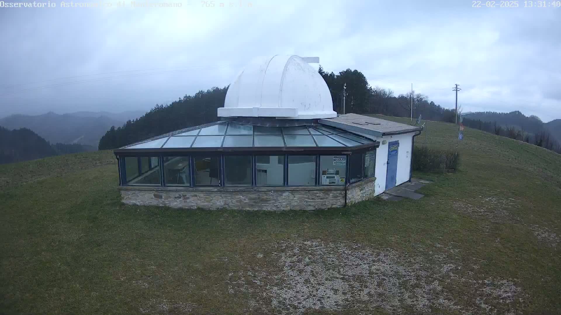 A stone building with a glass sunroom and a white dome on top sits on a grassy hill overlooking a hazy, overcast landscape.