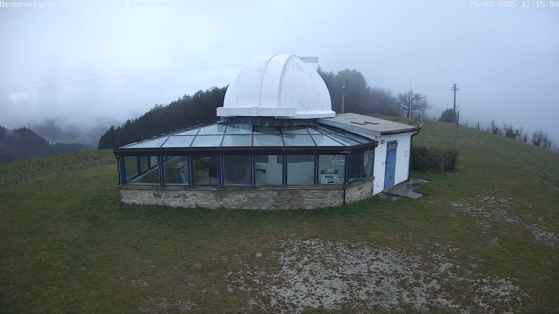 A stone building with a glass conservatory and a white dome sits on a grassy hill in foggy weather.